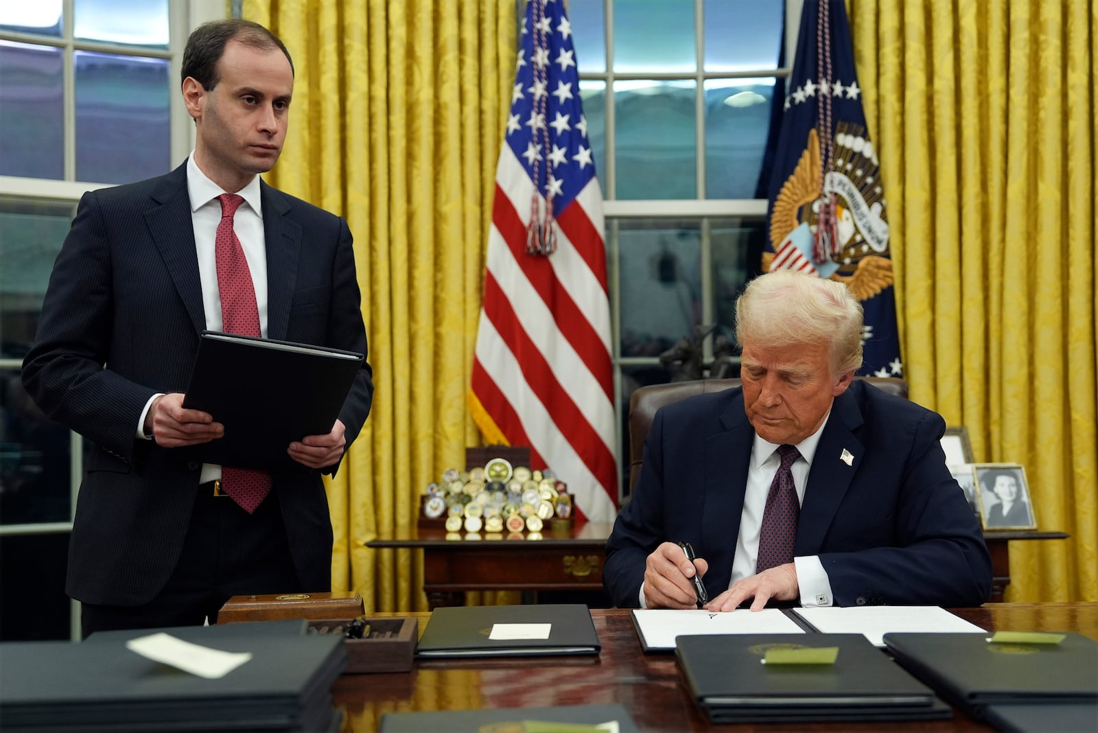 President Donald Trump signs an executive order to create the Department of Government Efficiency (DOGE) in the Oval Office of the White House, Monday, Jan. 20, 2025, in Washington, as White House staff secretary Will Scharf watches. (AP Photo/Evan Vucci)