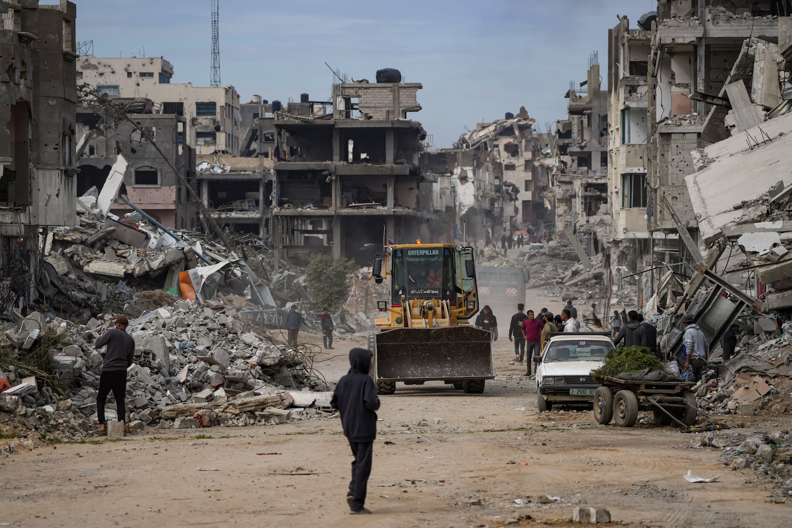 Palestinians watch as a bulldozer clears the rubble of destroyed residential buildings damaged by the Israeli air and ground offensive in Bureij, central Gaza Strip, Wednesday, Jan. 22, 2025. (AP Photo/Abdel Kareem Hana)