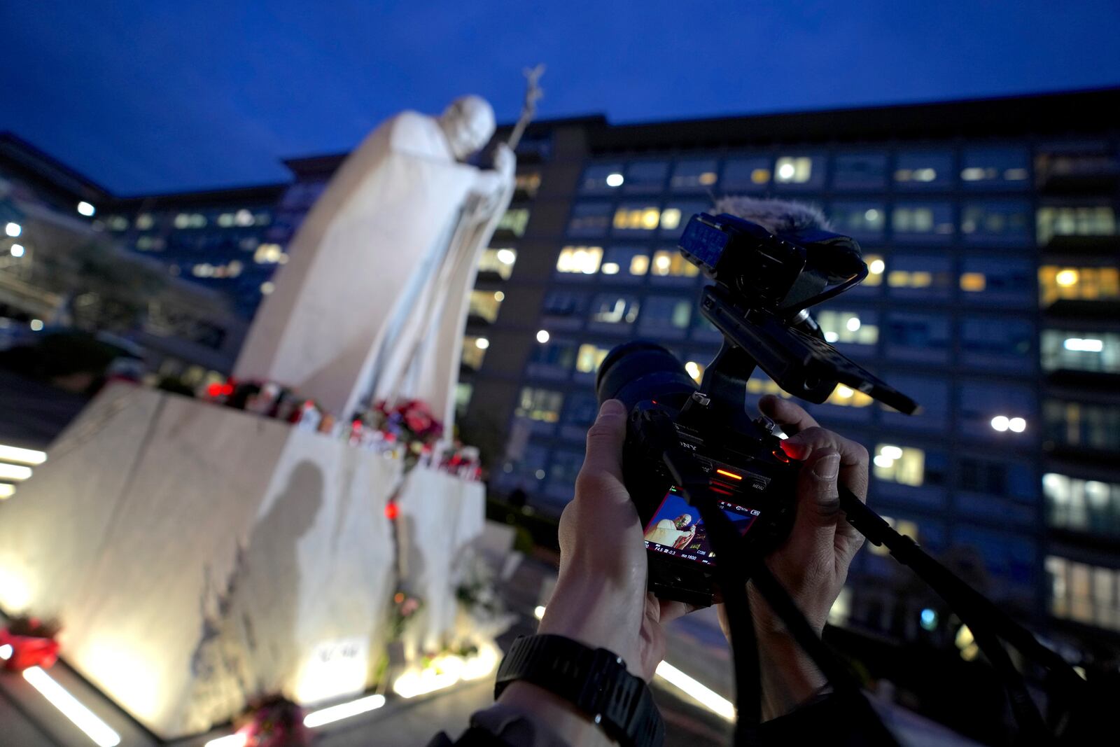 A cameraman scans a marble statue of late Pope John Paul II outside the Agostino Gemelli Polyclinic in Rome where Pope Francis is being treated for pneumonia, Thursday, Feb. 20, 2025. (AP Photo/Domenico Stinellis)