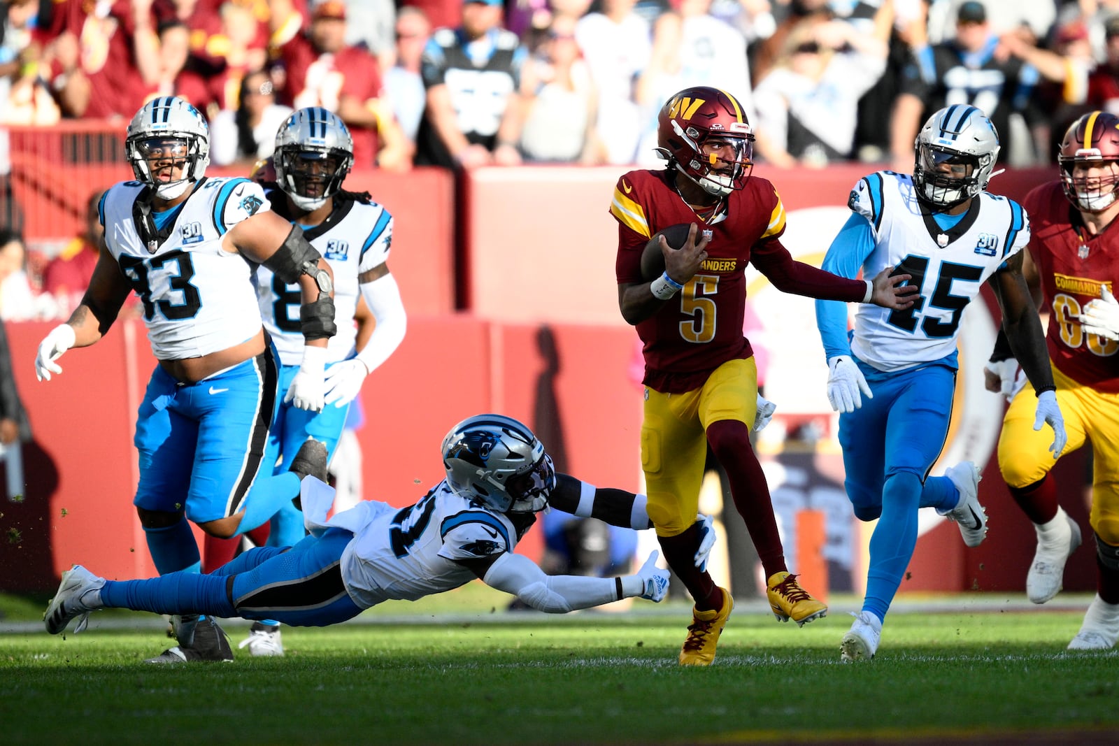 Washington Commanders quarterback Jayden Daniels (5) runs from Carolina Panthers safety Nick Scott (21) and linebacker Marquis Haynes Sr. (45) during the first half of an NFL football game, Sunday, Oct. 20, 2024, in Landover, Md. (AP Photo/Nick Wass)