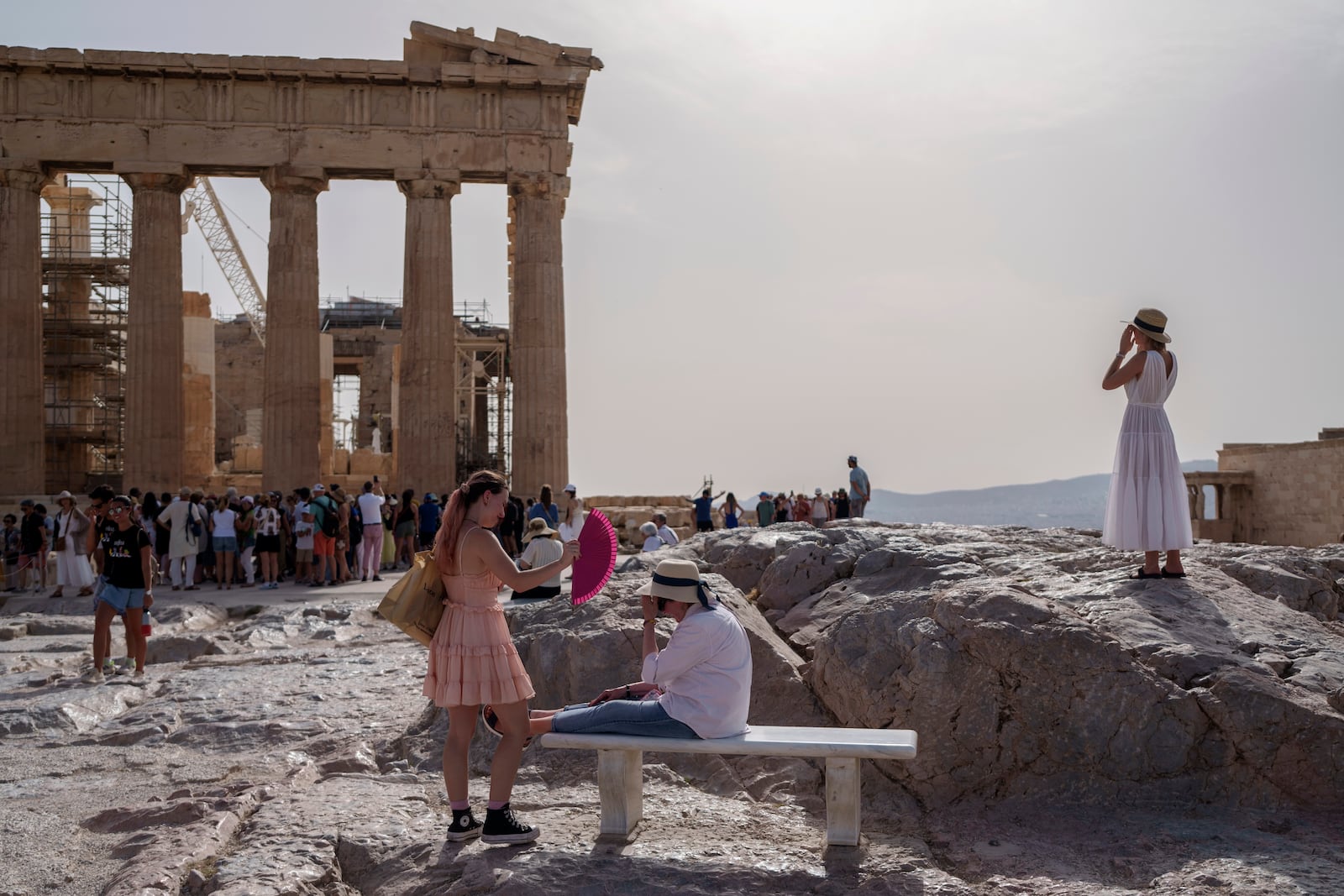 FILE - A tourist uses a hand fan to cool down another one sitting on a bench in front of the Parthenon at the ancient Acropolis, in Athens, June 12, 2024. (AP Photo/Petros Giannakouris, File)