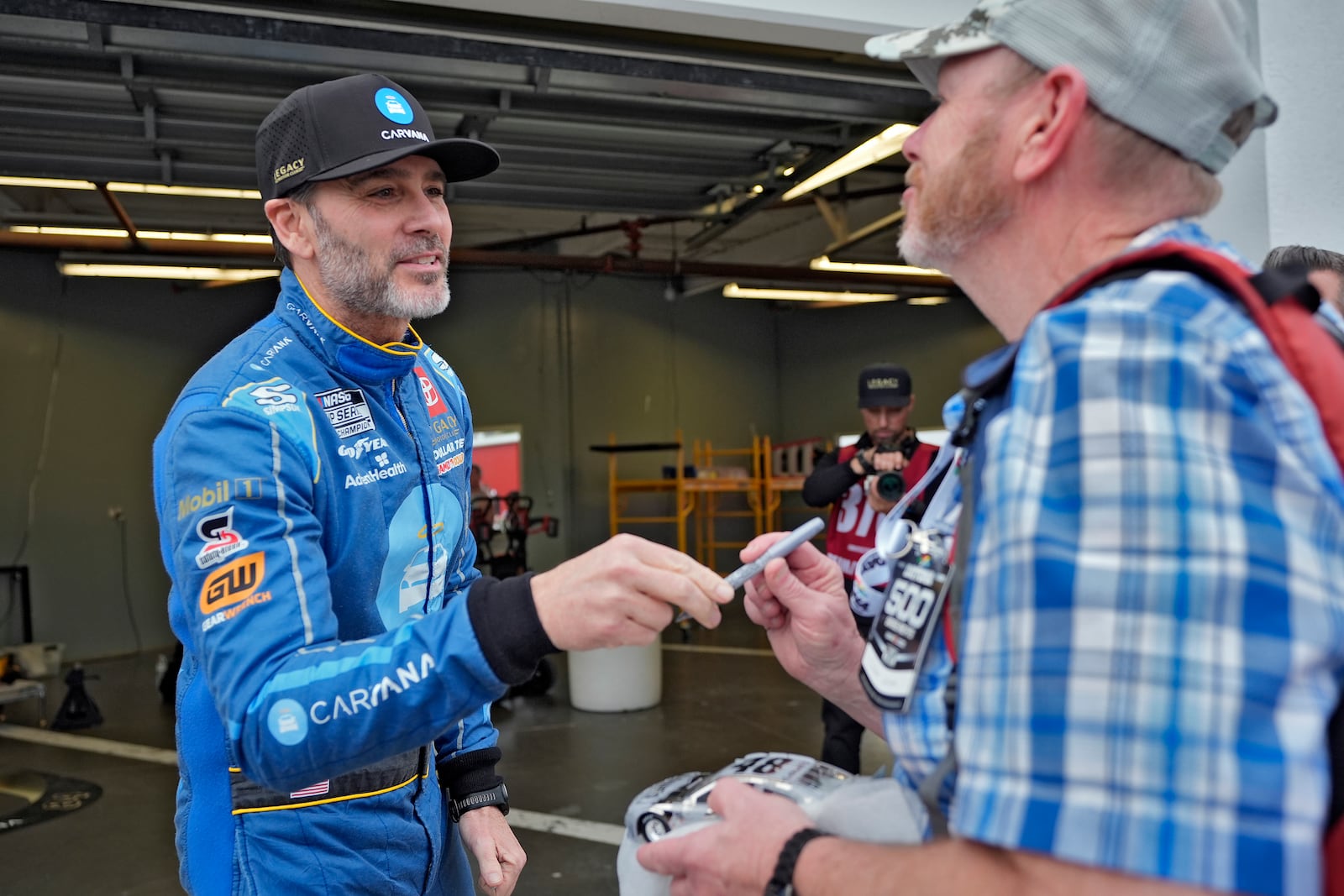 Jimmie Johnson, left, talks to a fan after signing an autograph before a practice for the NASCAR Daytona 500 auto race Friday, Feb. 14, 2025, at Daytona International Speedway in Daytona Beach, Fla. (AP Photo/Chris O'Meara)