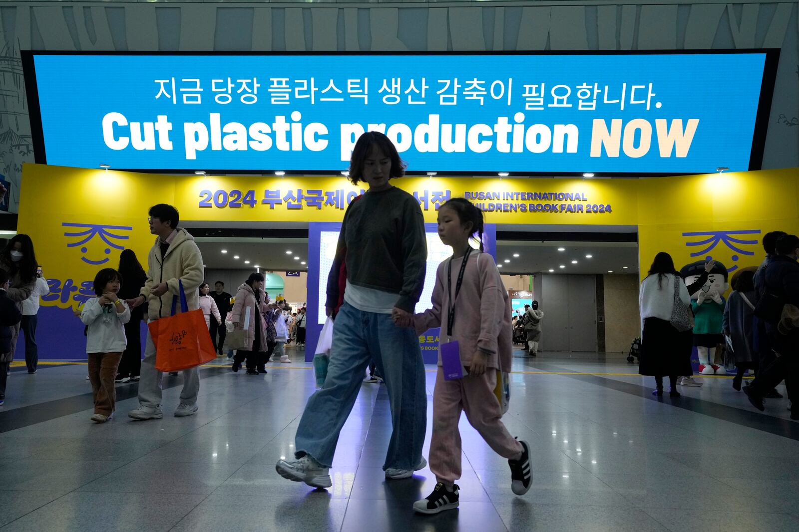 FILE - People pass by a sign calling for a reduction in plastic production near the venue for the fifth session of the Intergovernmental Negotiating Committee on Plastic Pollution in Busan, South Korea, Nov. 30, 2024. (AP Photo/Ahn Young-joon)