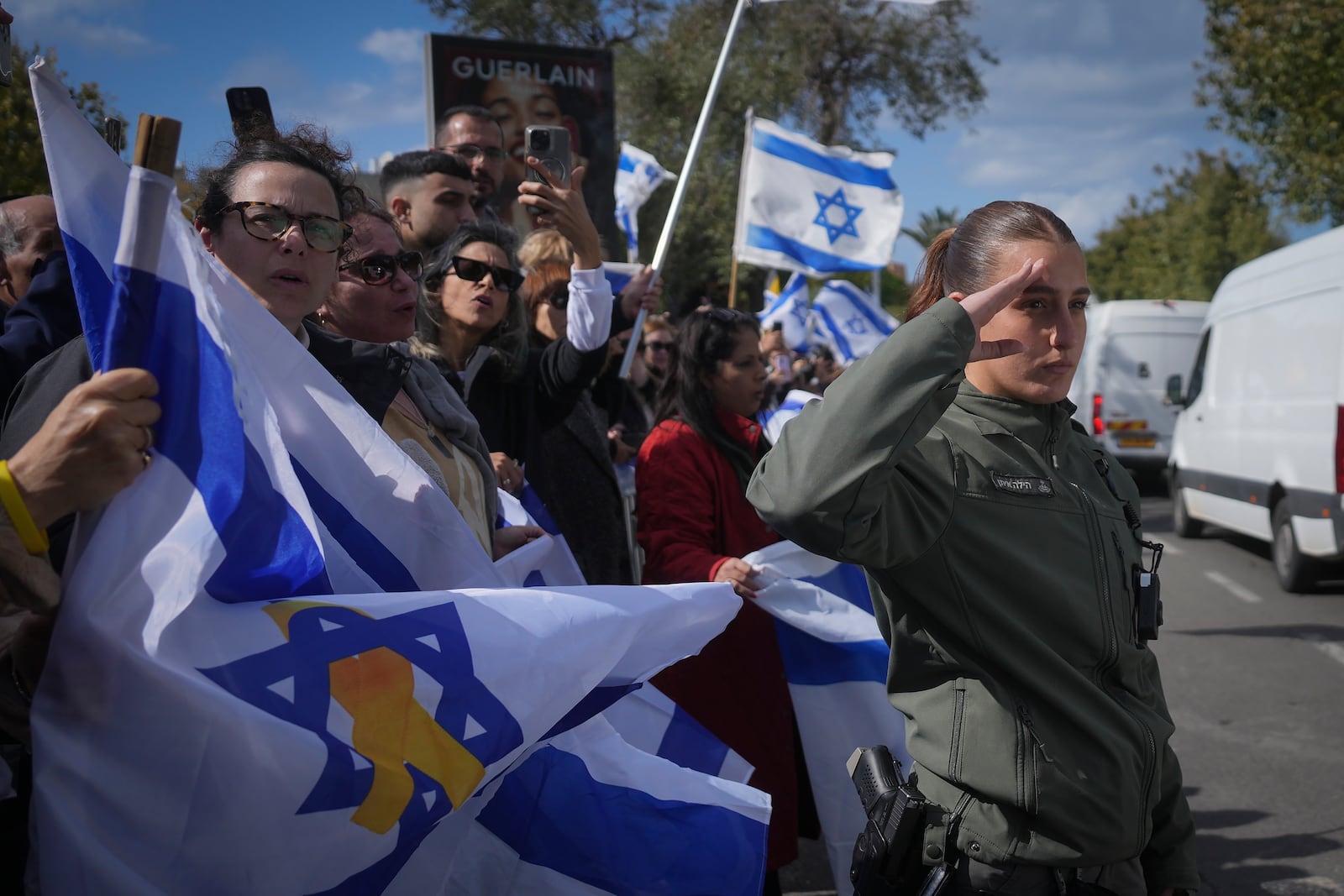 An Israeli border policewoman salutes as a convoy carrying the coffins of four Israeli hostages, including a mother and her two children, arrives at the Abu Kabir Forensic Institute in Tel Aviv, Israel, Thursday Feb. 20, 2025 after the bodies were handed over by Palestinian militant groups in Gaza.(AP Photo/Ohad Zwigenberg)