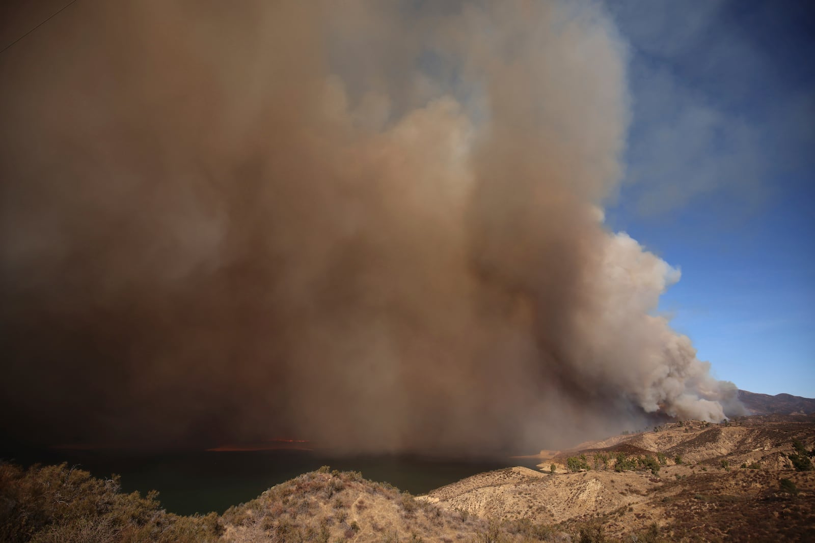 Plumes of smoke caused by the Hughes Fire rise over Lake Castaic, Calf., Wednesday, Jan. 22, 2025. (AP Photo/Ethan Swope)