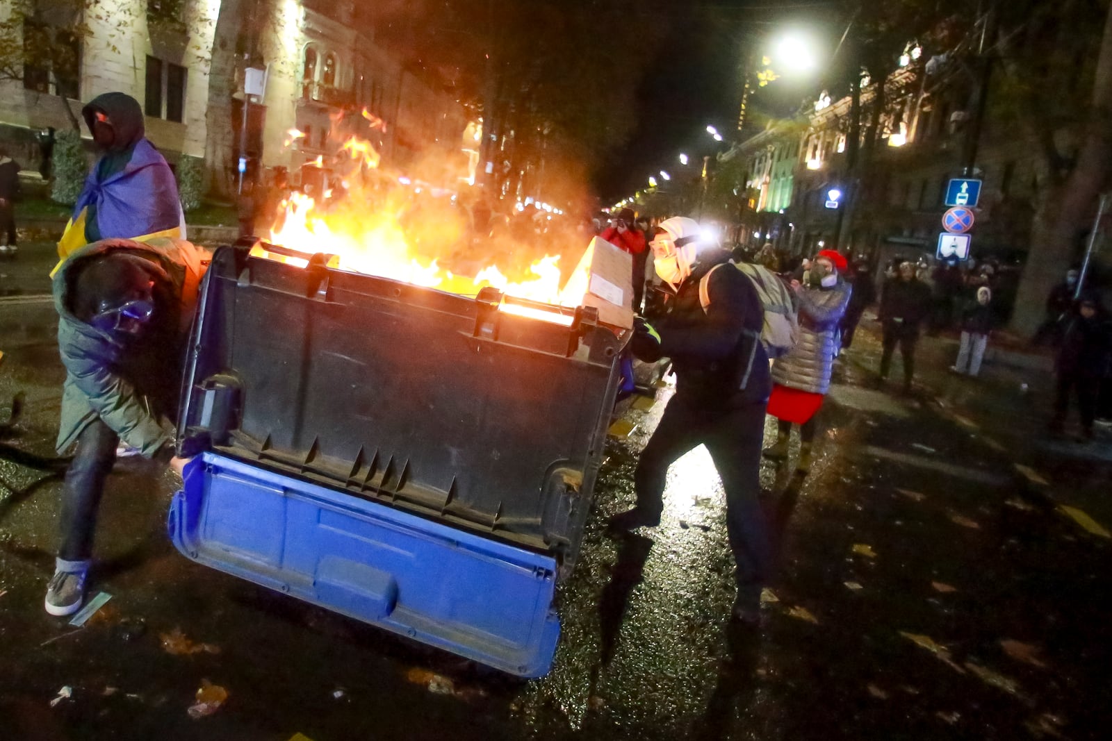 A group of protesters move a burning garbage container pouring into the streets following Georgian Prime Minister Irakli Kobakhidze's announcement, rallying outside the parliament building in Tbilisi, Georgia, on Friday, Nov. 29, 2024. (AP Photo/Zurab Tsertsvadze)