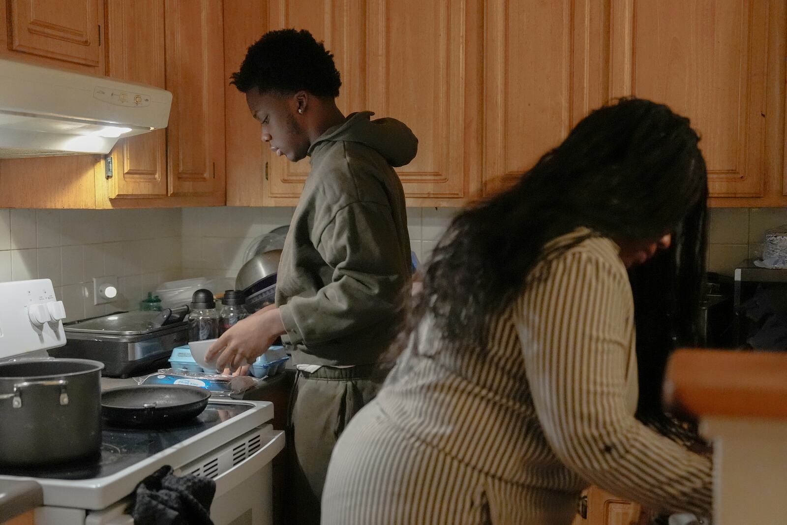 Camden Lee, left, cooks breakfast while his mom Chee Chee Brock, right, gets ready for work, Tuesday, Jan. 28, 2025, in the Brooklyn borough of New York. (AP Photo/Julia Demaree Nikhinson)