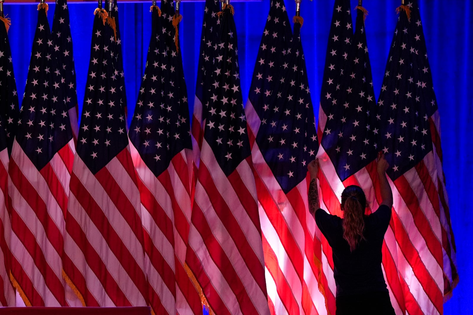 FILE - A worker adjusts U.S. flags on the stage ahead of an election night watch party for Republican presidential nominee, former President Donald Trump, in West Palm Beach, Fla., Nov. 5, 2024. (AP Photo/Julia Demaree Nikhinson, File)