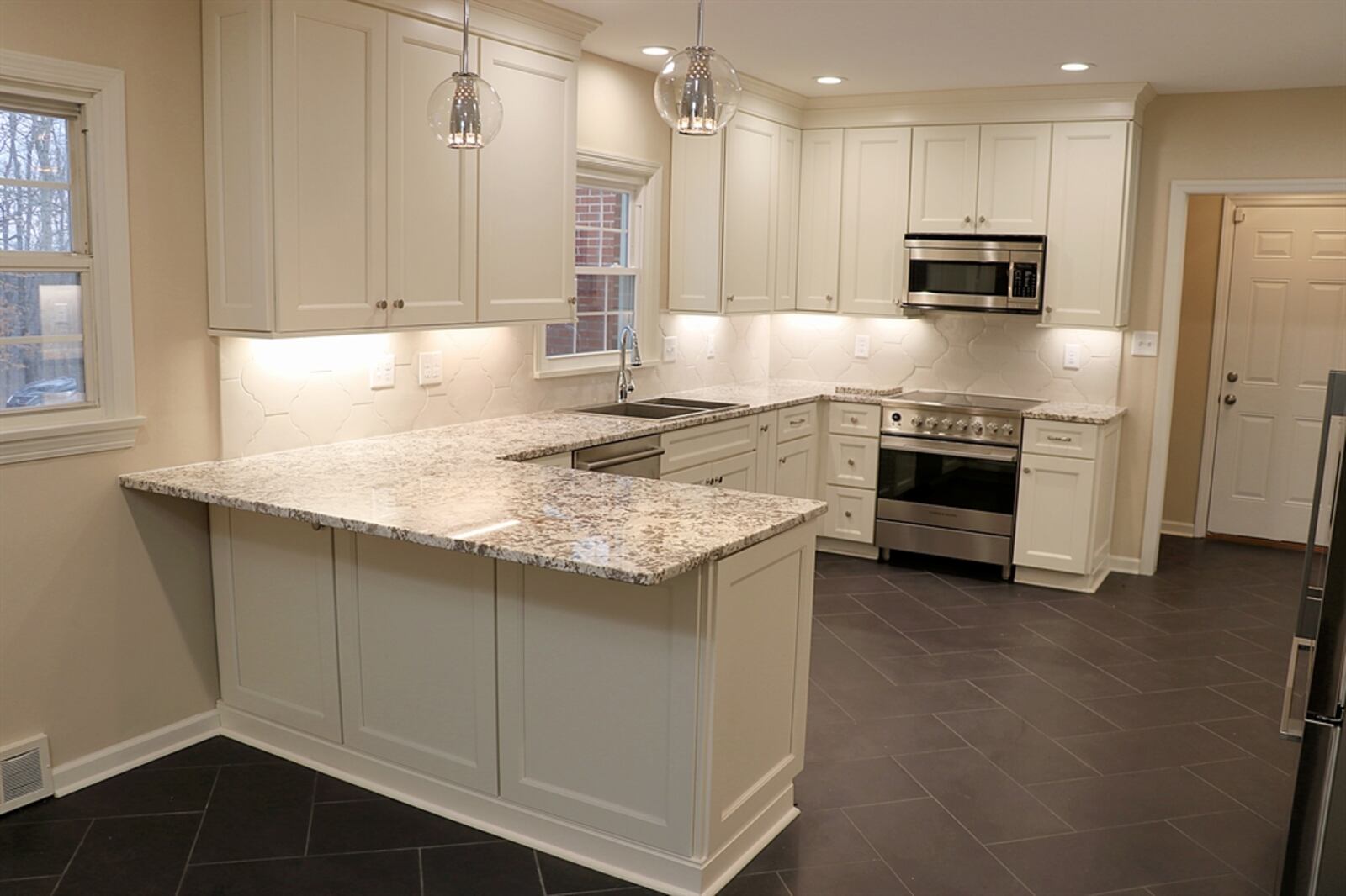 The redesigned kitchen has white cabinetry with soft-close doors and light granite counters. A window is above the double sink and under-cabinet lighting shows off the ornate white ceramic-tile details. A double door pantry cabinet has pull-out shelves, and a planning niche has open shelves. The peninsula counter has storage and an extended counter for seating.  Contributed photos