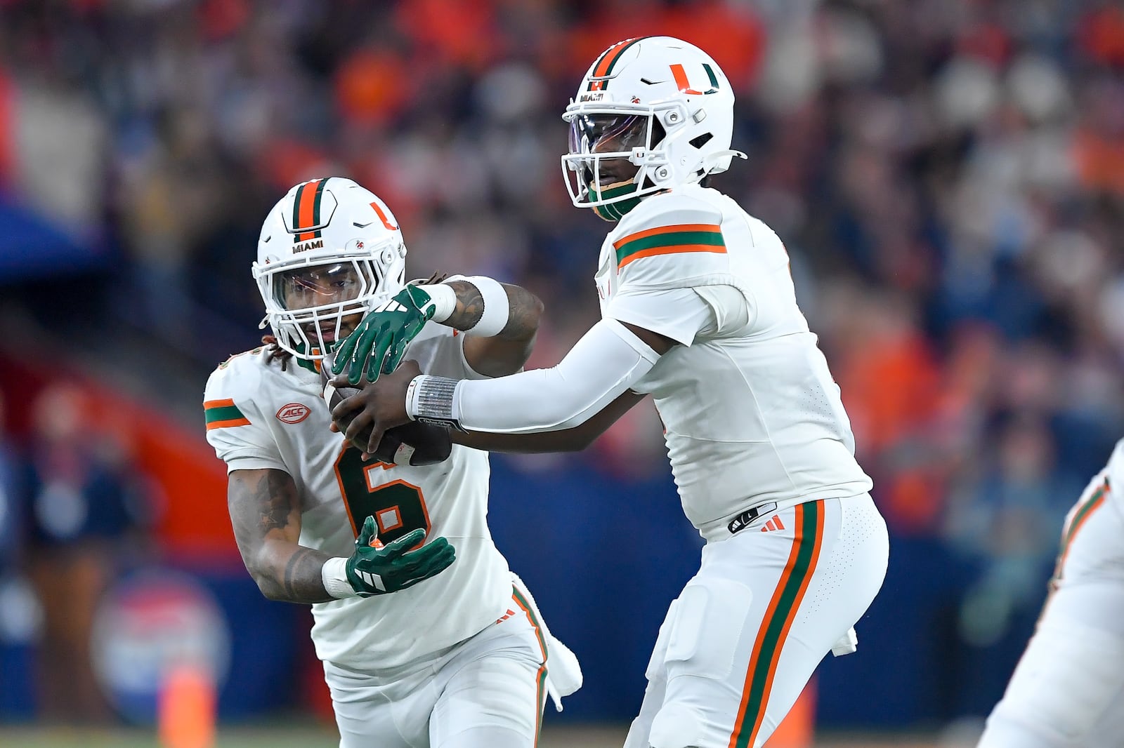 Miami quarterback Cam Ward, right, hands off to running back Damien Martinez during the first half of an NCAA football game against Syracuse on Saturday, Nov. 30, 2024 in Syracuse, N.Y. (AP Photo/Adrian Kraus)