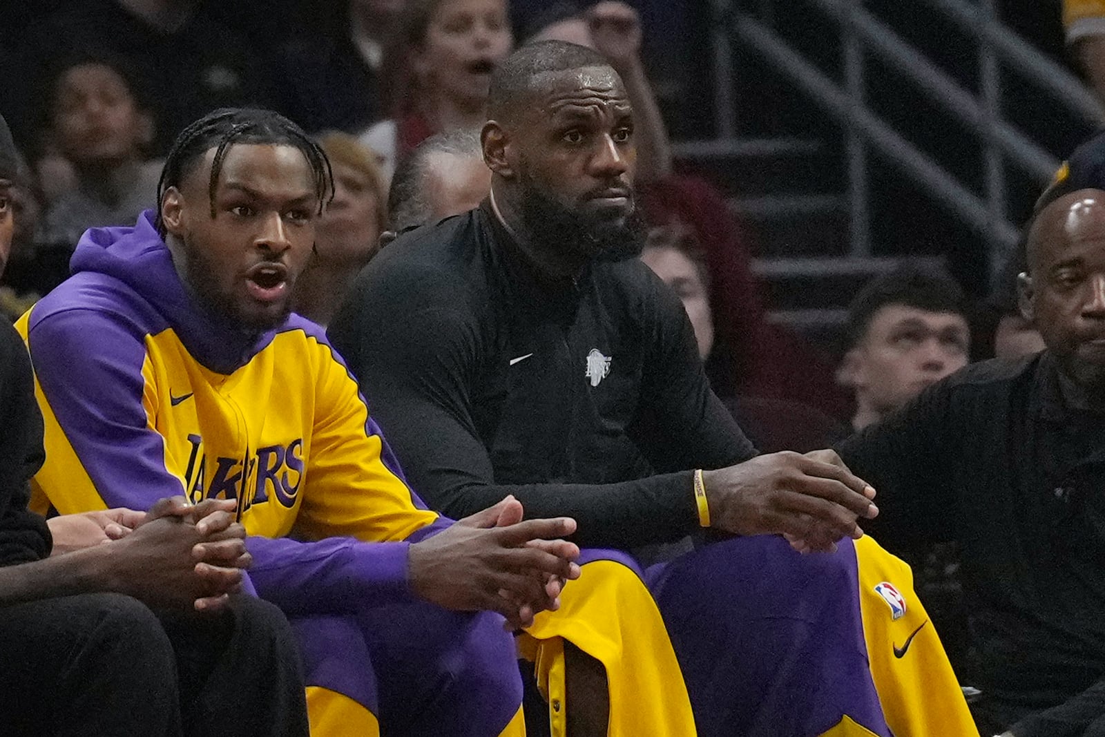 Los Angeles Lakers guard Bronny James, left, and forward LeBron James, right, watch from the bench in the first half of an NBA basketball game against the Cleveland Cavaliers, Wednesday, Oct. 30, 2024, in Cleveland. (AP Photo/Sue Ogrocki)