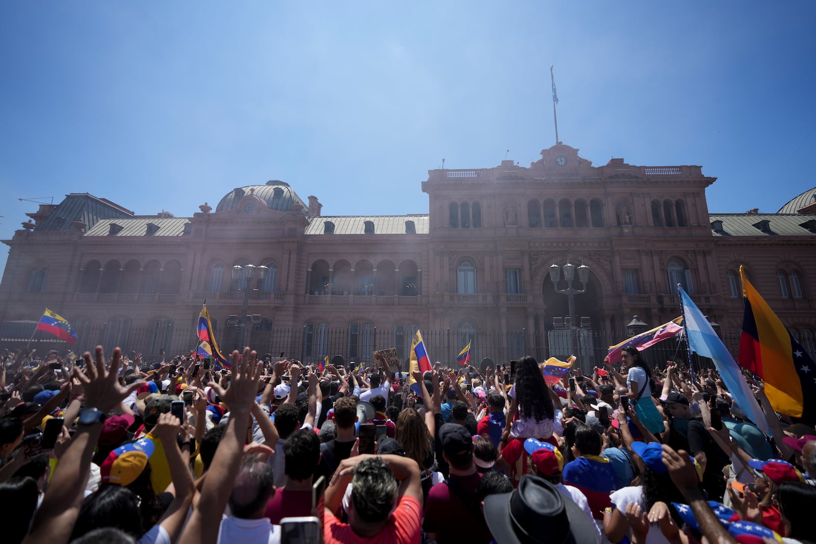 People watch Venezuela's opposition leader Edmundo Gonzalez Urrutia and Argentine President Javier Milei wave to supporters from the government house balcony in Buenos Aires, Argentina, Saturday, Jan. 4, 2025. Gonzalez, who claims he won the 2024 presidential election and is recognized by some countries as the legitimate president-elect, traveled from exile in Madrid to Argentina. (AP Photo/Natacha Pisarenko)