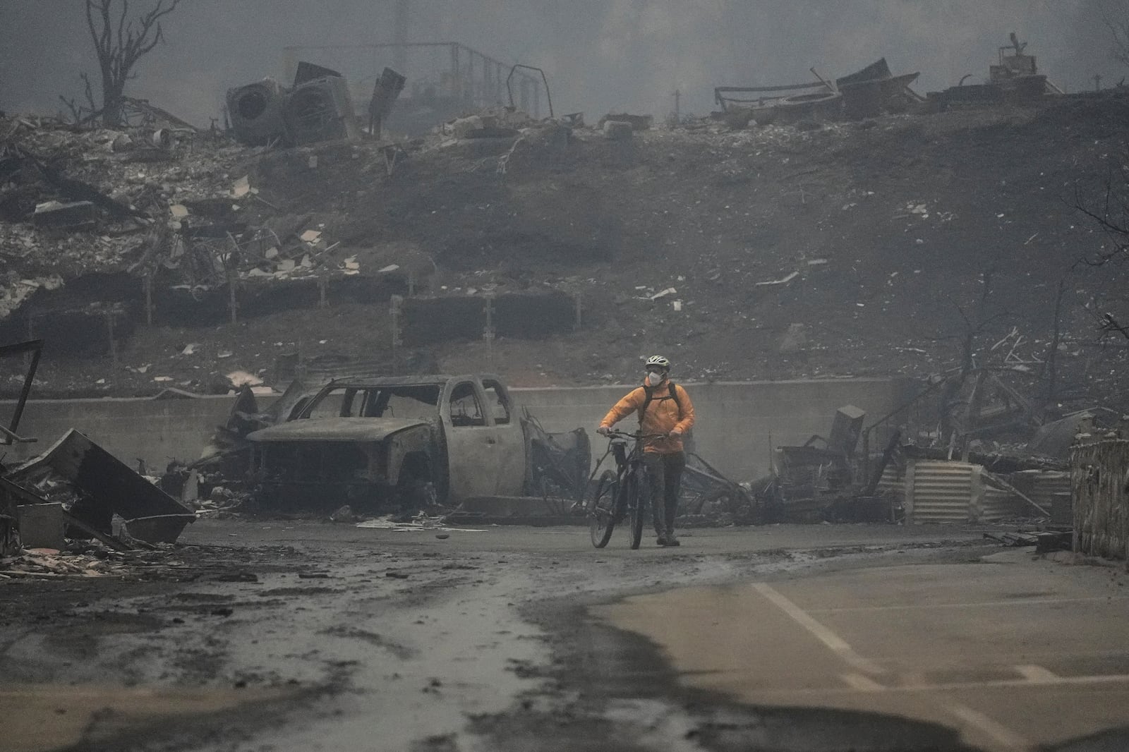 A man walks his bike among the ruins left behind by the Palisades Fire in the Pacific Palisades neighborhood of Los Angeles, Wednesday, Jan. 8, 2025. (AP Photo/Damian Dovarganes)