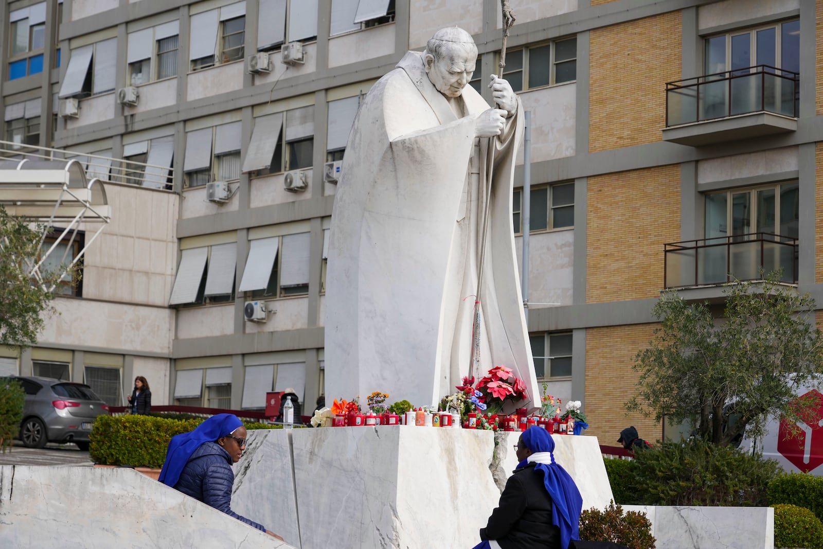 Nuns sit next to a statue of Pope John Paul II in front of the Agostino Gemelli Polyclinic, in Rome, Monday, Feb. 17, 2025, where Pope Francis has been hospitalized to undergo some necessary diagnostic tests and to continue his ongoing treatment for bronchitis. (AP Photo/Andrew Medichini)