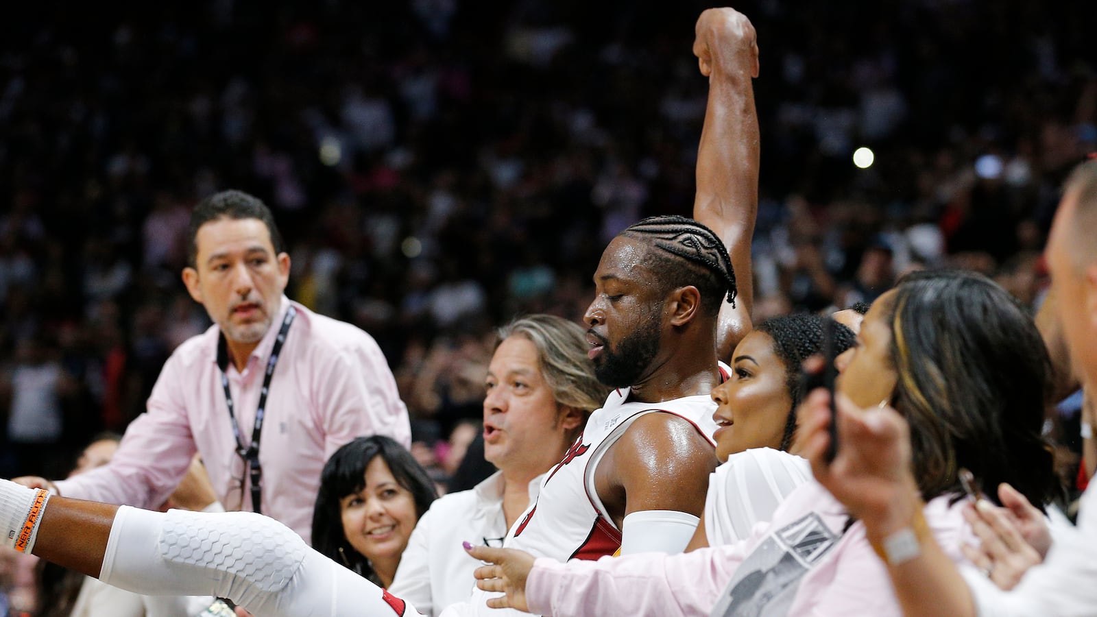 Dwyane Wade #3 of the Miami Heat falls into friends John Legend and Chrissy Teigen and wife Gabrielle Union after shooting a three pointer against the Philadelphia 76ers during the second half at American Airlines Arena on April 09, 2019 in Miami.