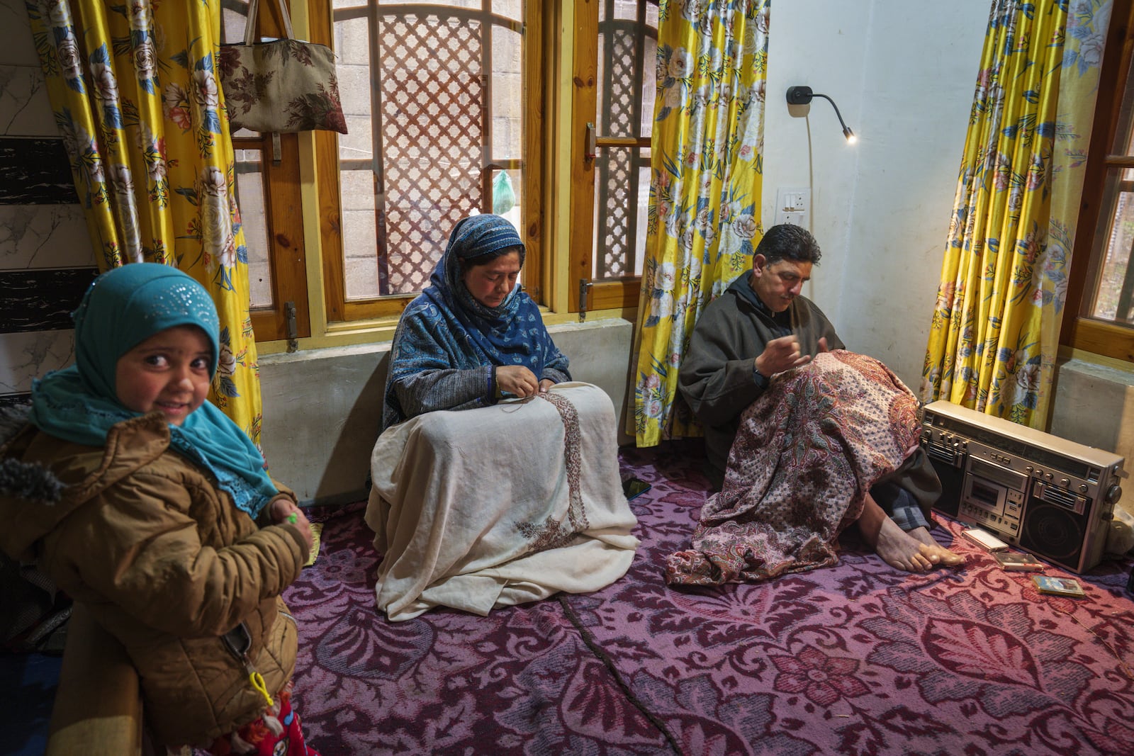 Manzoor Ahmad Bhat, right, along with his wife Mymoona Manzoor, embroiders Kashmiri shawls as her niece Aksa, left, looks on while they listen to Kashmiri Sofi music on a tape recorder inside their house in Yarigund village southwest of Srinagar, Indian controlled Kashmir, Thursday, Feb. 20, 2025. (AP Photo/Dar Yasin)