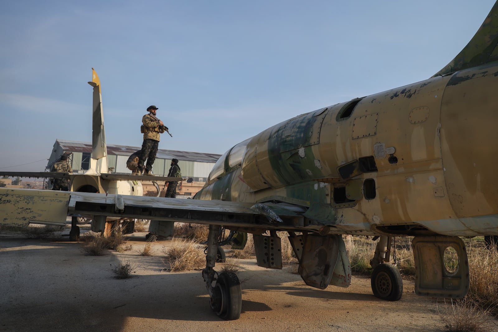 Syrian opposition fighters stand on the wings of an old aircraft at the Al-Nayrab military airport after they took control of the facility in the outskirts of Aleppo, Syria, Monday, Dec. 2, 2024. .(AP Photo/Omar Albam)