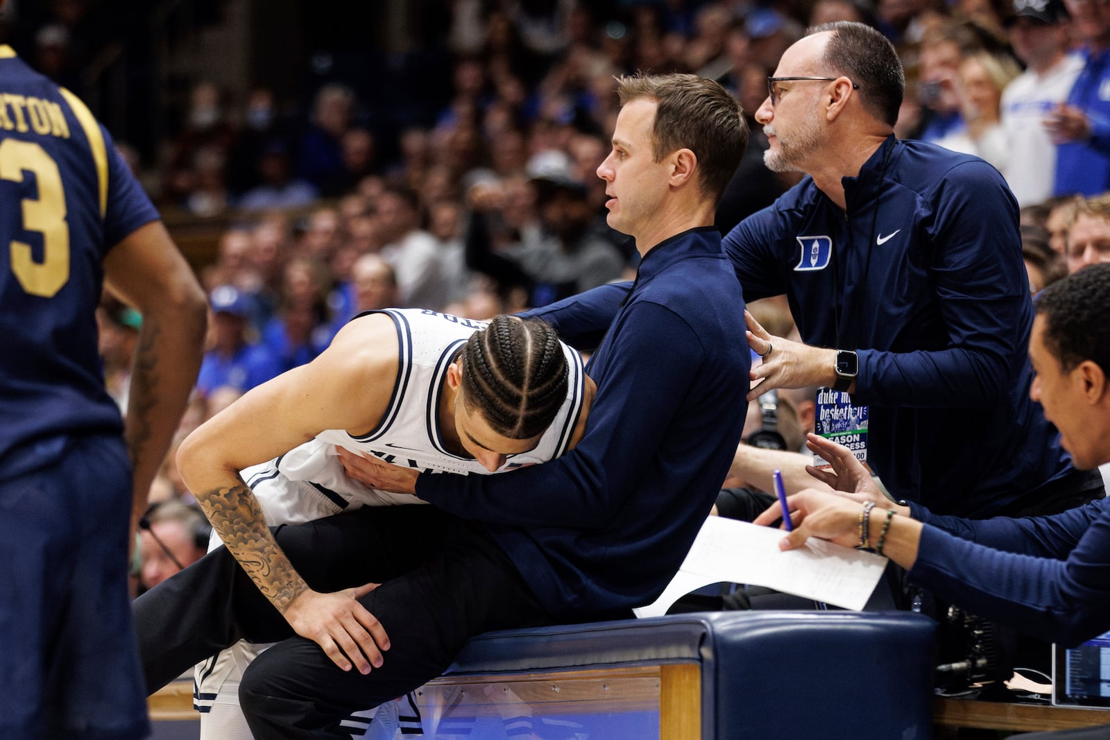 Duke's Tyrese Proctor, left, falls into Duke head coach Jon Scheyer, right, after chasing a loose ball during the first half of an NCAA college basketball game against Notre Dame in Durham, N.C., Saturday, Jan. 11, 2025. (AP Photo/Ben McKeown)