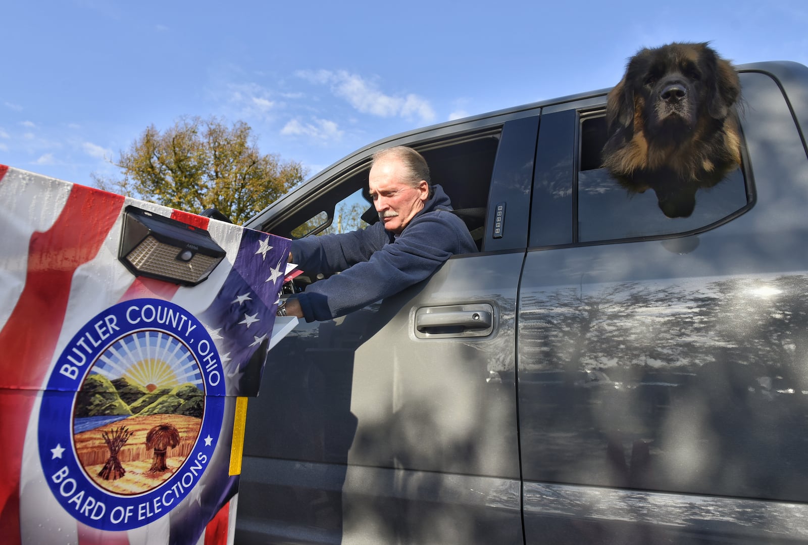 Jim Gau places his ballot in the drop box as his dog, Gunner, sticks his head out of the window at the Butler County Board of Elections Thursday, October 22, 2020 in Hamilton. NICK GRAHAM / STAFF