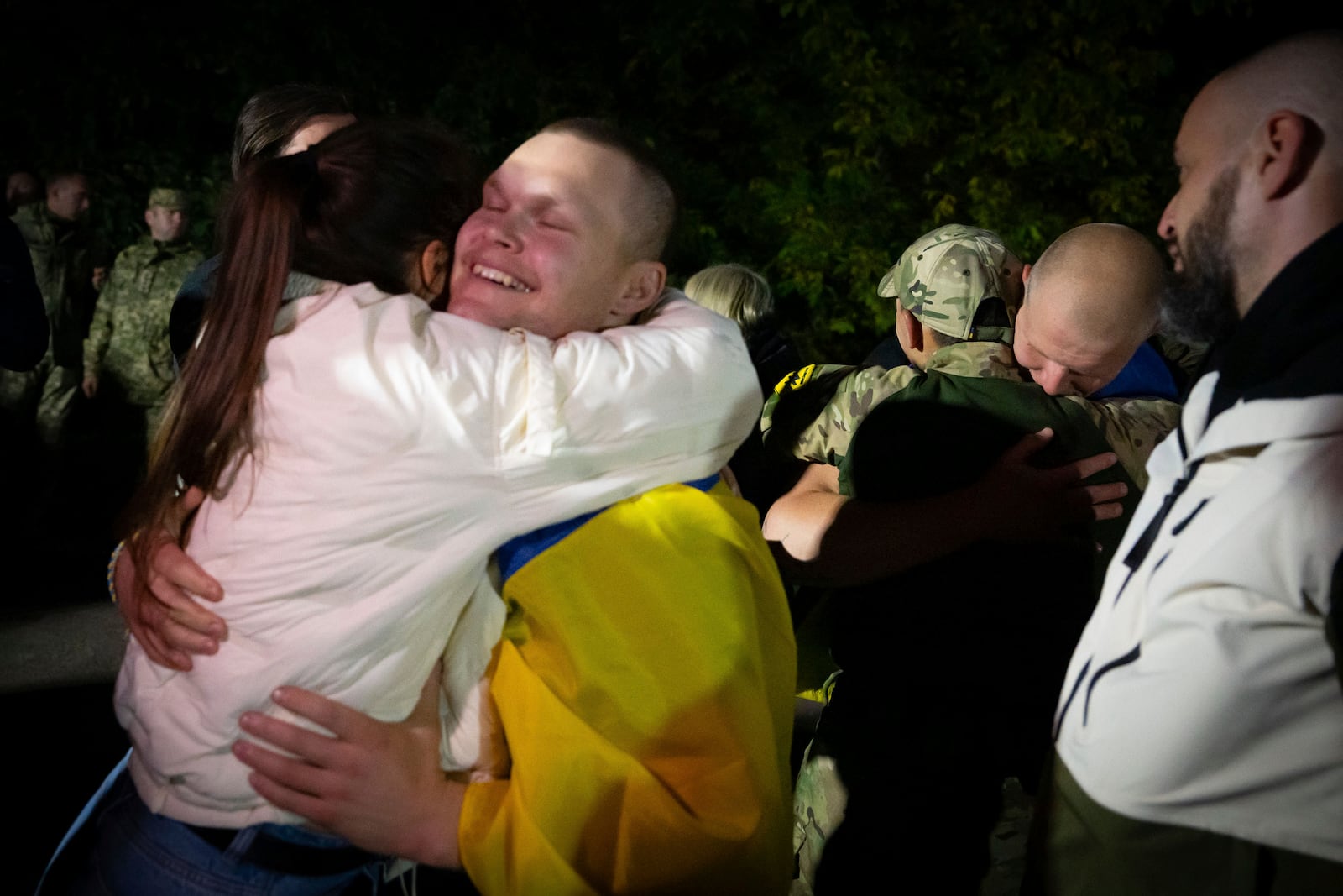 In this photo provided by the Press Service of the President of Ukraine on Oct. 19, 2024, a Ukrainian serviceman covered with a national flag hugs his relative after returning from captivity during a POWs exchange in an undisclosed location, Ukraine. (Press Service of the President of Ukraine via AP)