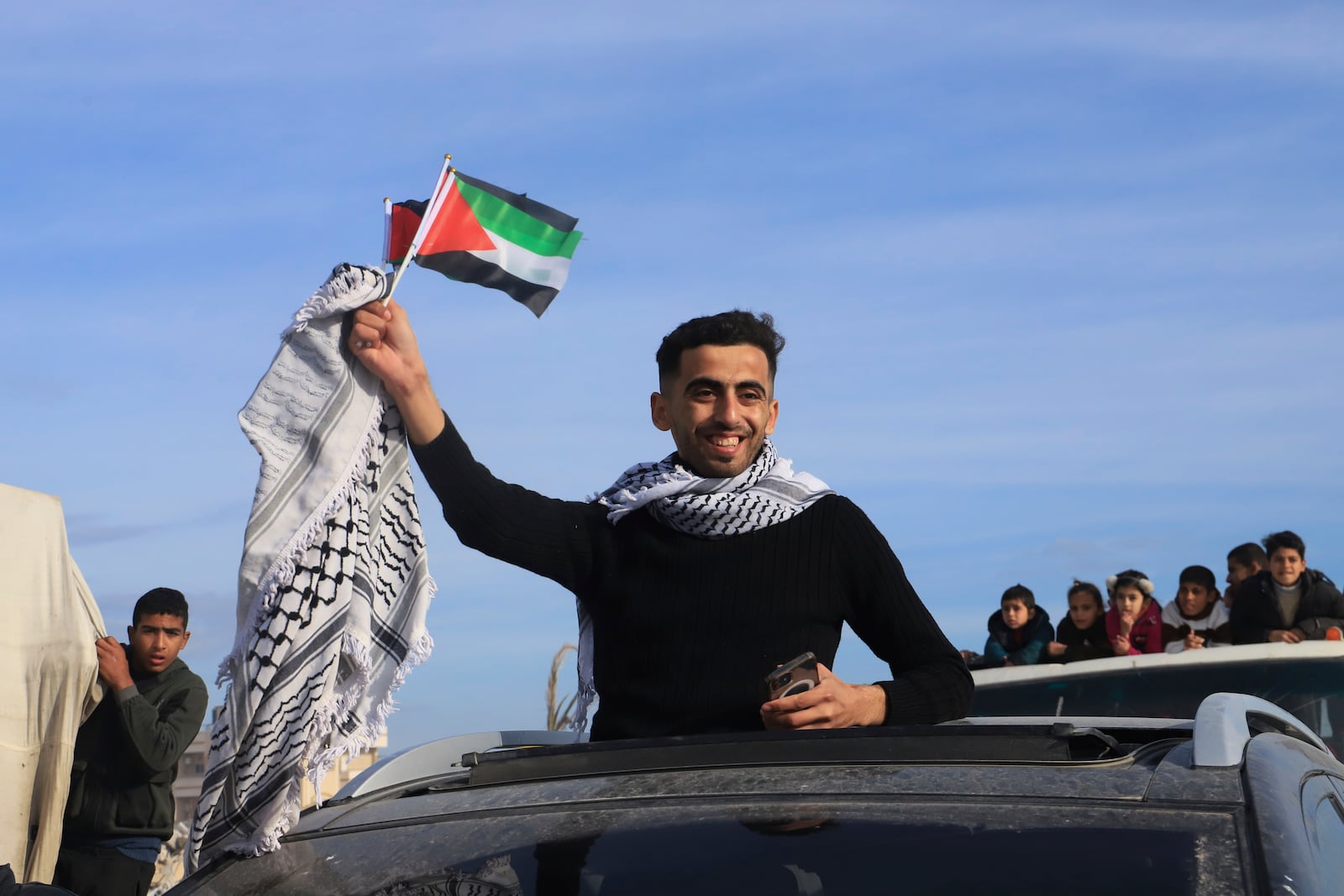 Displaced Palestinians wave the Palestinian flag as they return to Rafah, while a ceasefire deal between Israel and Hamas went into effect, in Rafah, Gaza Strip, Sunday, Jan. 19, 2025. (AP Photo/Mariam Dagga)