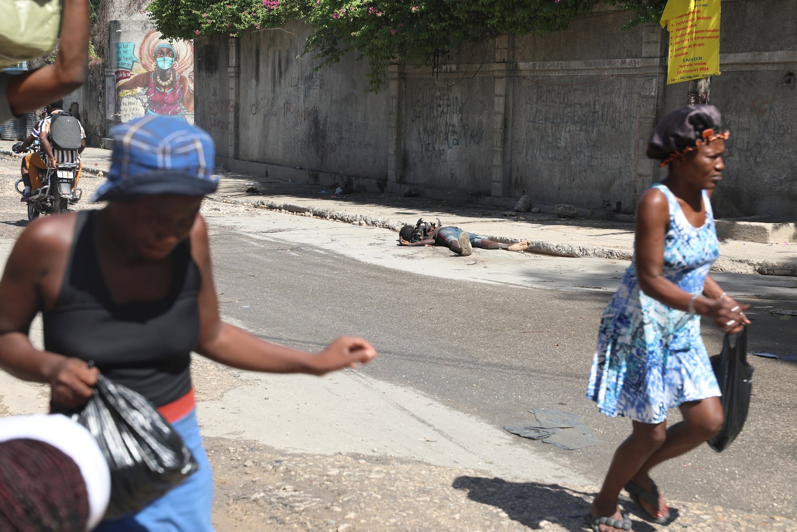 Pedestrians rush past the decomposing body of a man left abandoned on a street in downtown Port-au-Prince, Haiti, Wednesday, Nov. 13, 2024. (AP Photo/Odelyn Joseph)