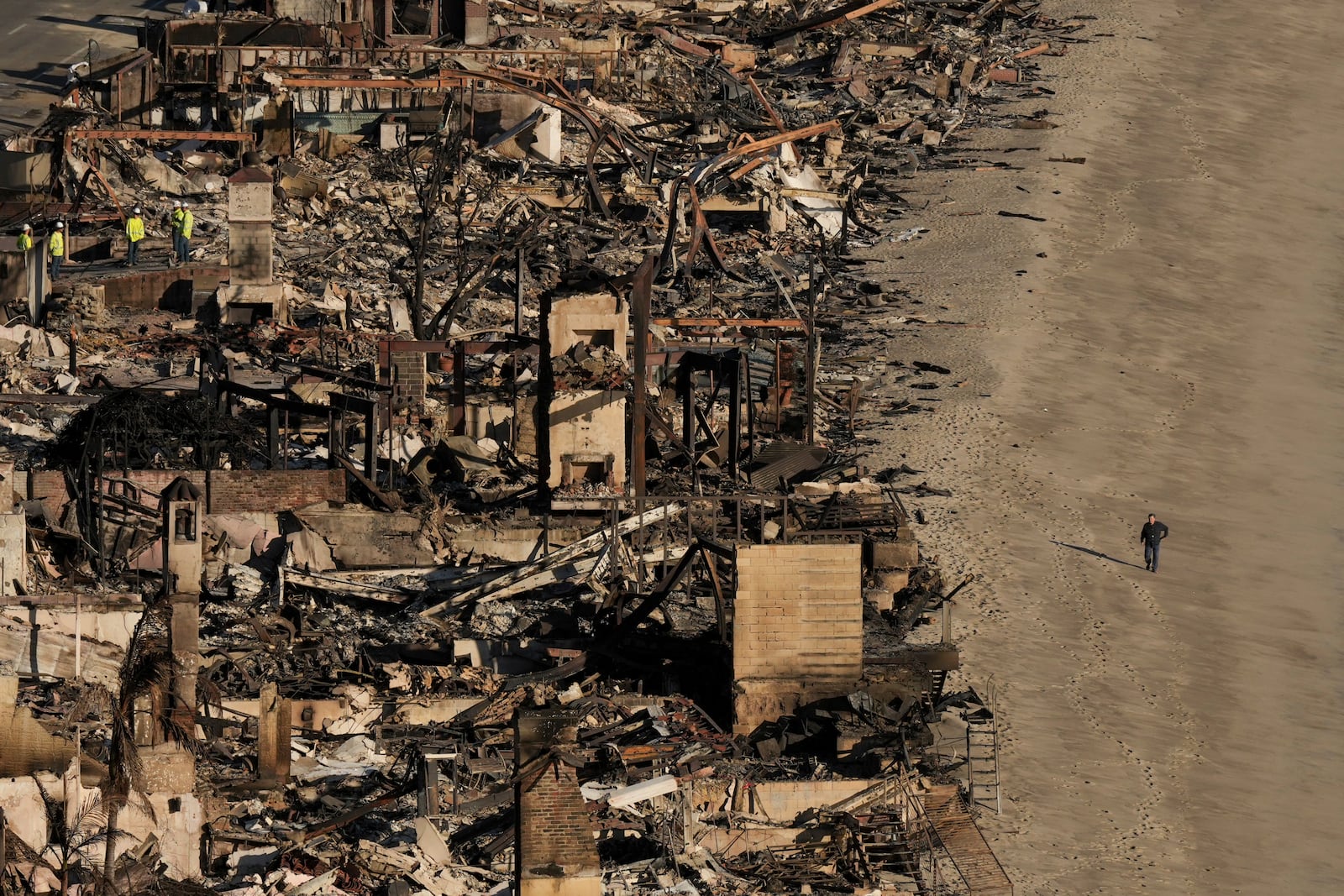 A person walks on the beach next to homes damaged by the Palisades Fire Thursday, Jan. 16, 2025 in Malibu, Calif. (AP Photo/Jae C. Hong)