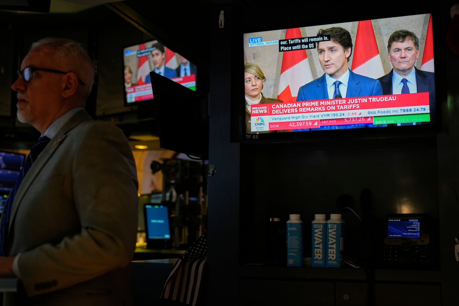 People work as a television displays a news conference by Canadian Prime Minister Justin Trudeau on the floor at the New York Stock Exchange in New York, Tuesday, March 4, 2025. (AP Photo/Seth Wenig)