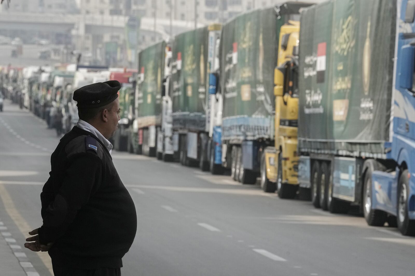 An Egyptian policeman stands in front of trucks of humanitarian aid at a parking point in Cairo, Egypt, as they wait to travel to cross the Rafah border crossing between Egypt and the Gaza Strip, Sunday, Jan. 26, 2025. (AP Photo/Amr Nabil)