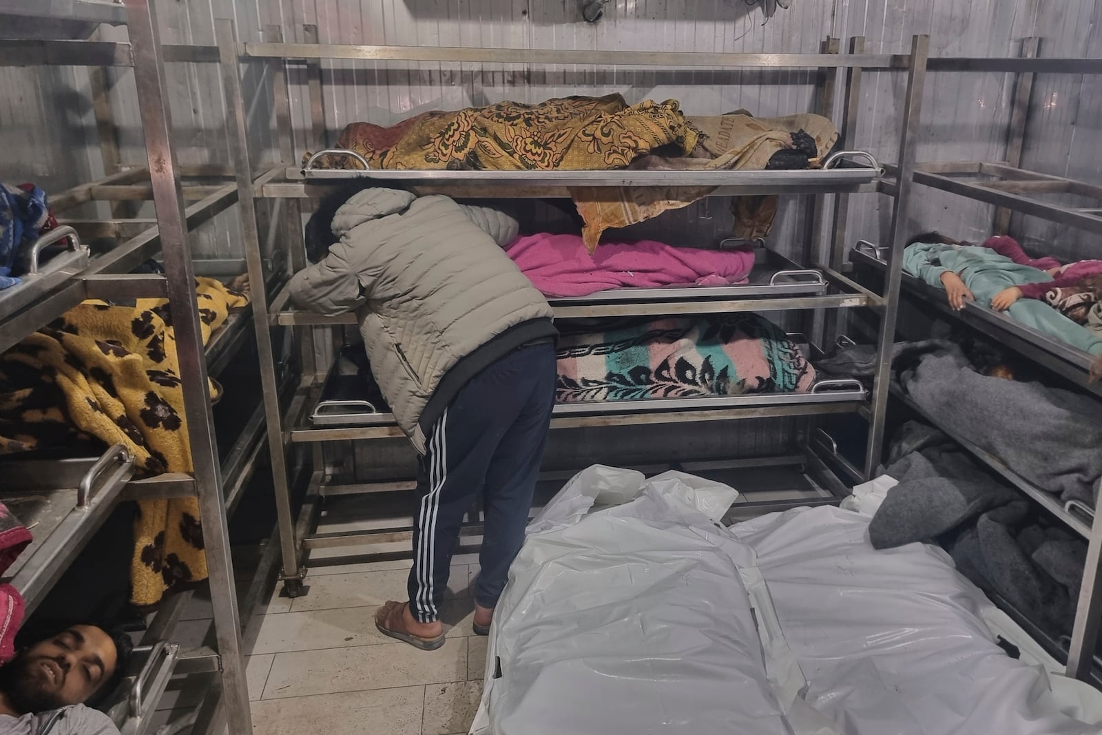 A man mourns over the body of a child, lying among other victims at the hospital morgue, following Israeli airstrikes in Khan Younis, southern Gaza Strip, Tuesday, March 18, 2025. (AP Photo/Mohammad Jahjouh)