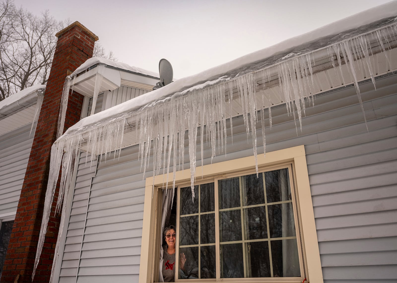 Claire Gagne peeks out from underneath an impressive curtain of icicles on her home in Lewiston, Maine, Thursday, Feb. 13, 2025. (Andree Kehn/Sun Journal via AP)