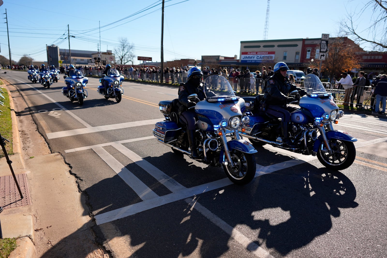 A police escort passes as the hearse carrying the flag-draped casket of former President Jimmy Carter approaches during a procession in downtown Plains, Ga., Saturday, Jan. 4, 2025. (AP Photo/Mike Stewart)