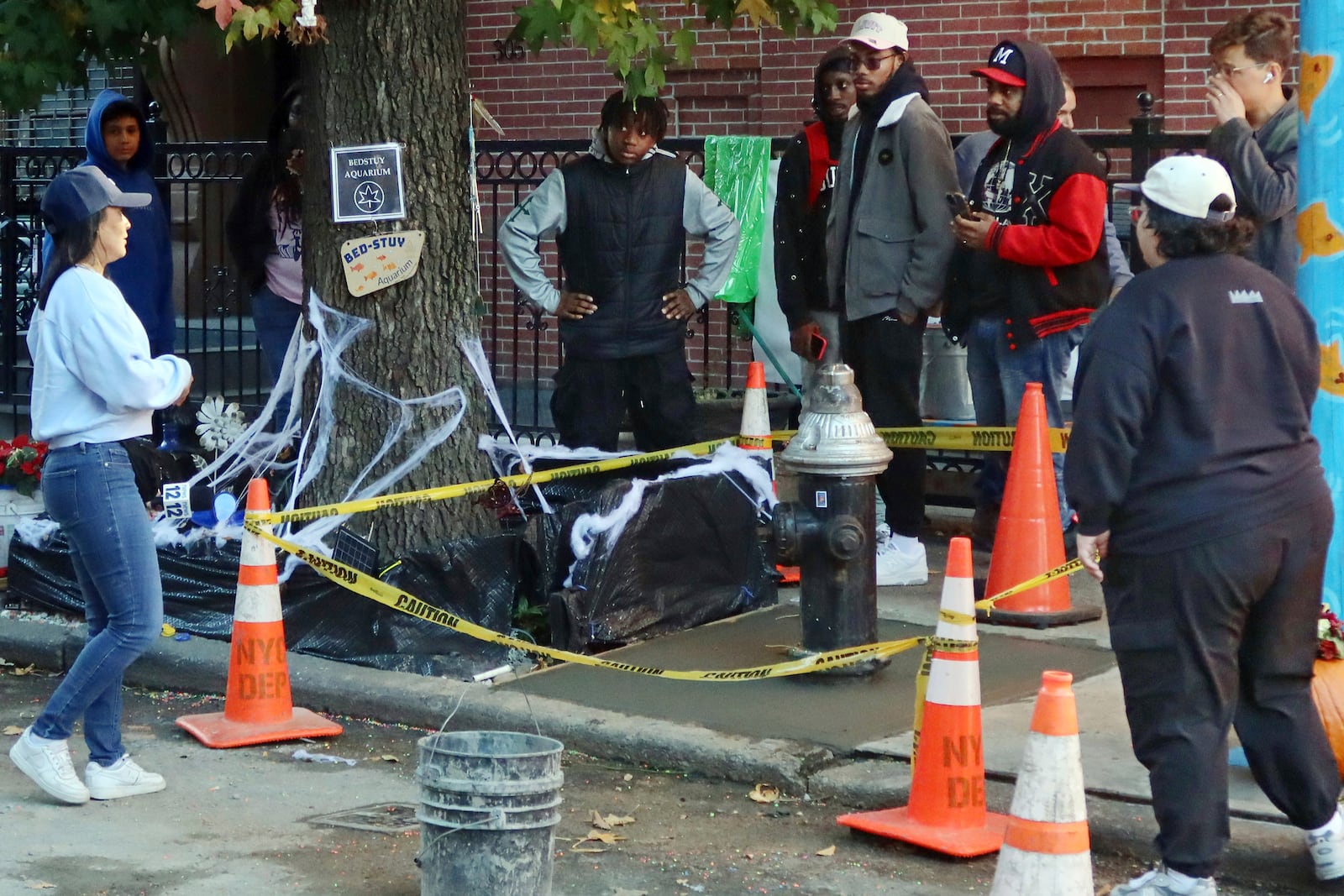 People gather at the yellow caution-taped area around a once leaky fire hydrant that became a makeshift aquarium goldfish pool, and now has been filled with concrete by the city, Friday, Oct. 25, 2024, in the Brooklyn borough of New York. (AP Photo/Cedar Attanasio)