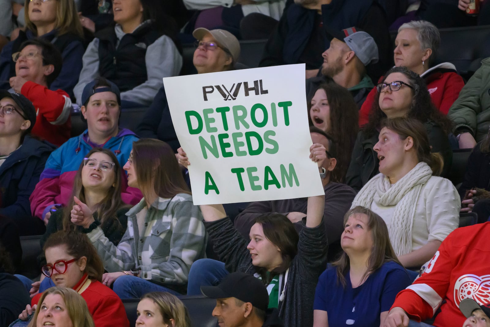 A fan holds a sign indicating a desire for an PWHL team to come to Detroit during the first period of a PWHL game between the New York Sirens and the Minnesota Frost, at Little Caesars Arena, in Detroit, Sunday, March 16, 2025. (David Guralnick/Detroit News via AP)