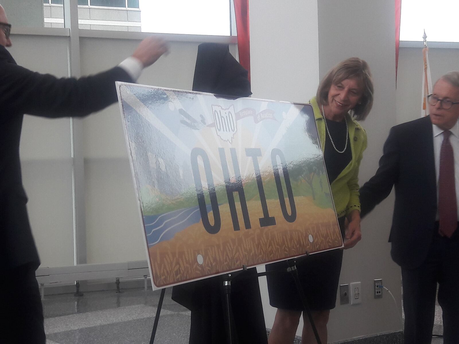 Gov. Mike DeWine (right), First Lady Fran DeWine and Bureau of Motor Vehicles Registrar Charles Norman (left) reveal the new "Sunrise in Ohio" standard license plate design Oct. 21, 2021.