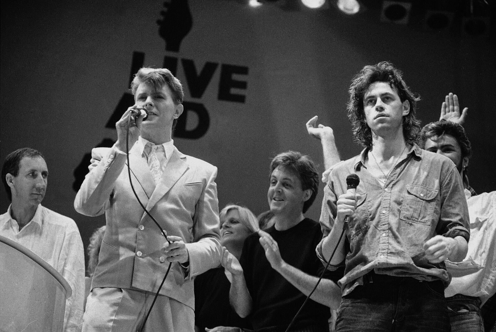 FILE -David Bowie, front left, and Bob Geldof, right right, appear at the end of the London part of the Live Aid famine relief concert at Wembley Stadium in London on July 13, 1985. (AP Photo/Joe Schaber, File)