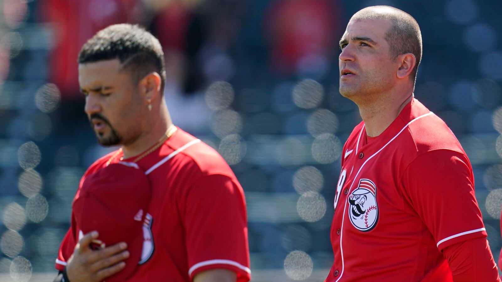 Cincinnati Reds' Eugenio Suarez, left, and Joey Votto, right, pause during the national anthem prior to a spring training baseball game against the Cleveland Indians Sunday, Feb. 28, 2021, in Goodyear, Ariz. (AP Photo/Ross D. Franklin)