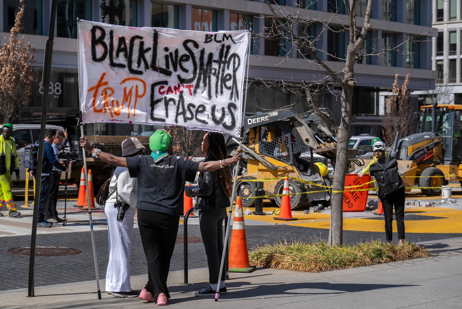 Nadine Seiler holds a sign saying "Black Lives Matter, Trump Can't Erase Us," Monday, March 10, 2025, in Washington, as demolition begins on the Black Lives Matter mural. (AP Photo/Jacquelyn Martin)