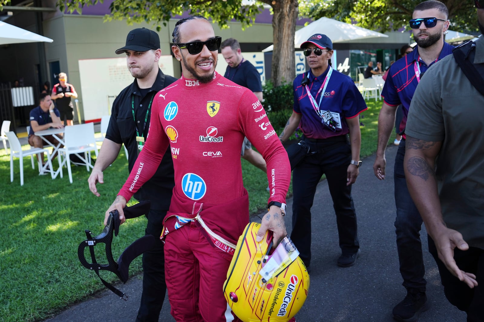 Ferrari driver Lewis Hamilton of Britain reacts as he walks through the F1 paddock ahead of the Australian Formula One Grand Prix at Albert Park, in Melbourne, Australia, Thursday, March 13, 2025. (AP Photo/Heath McKinley)