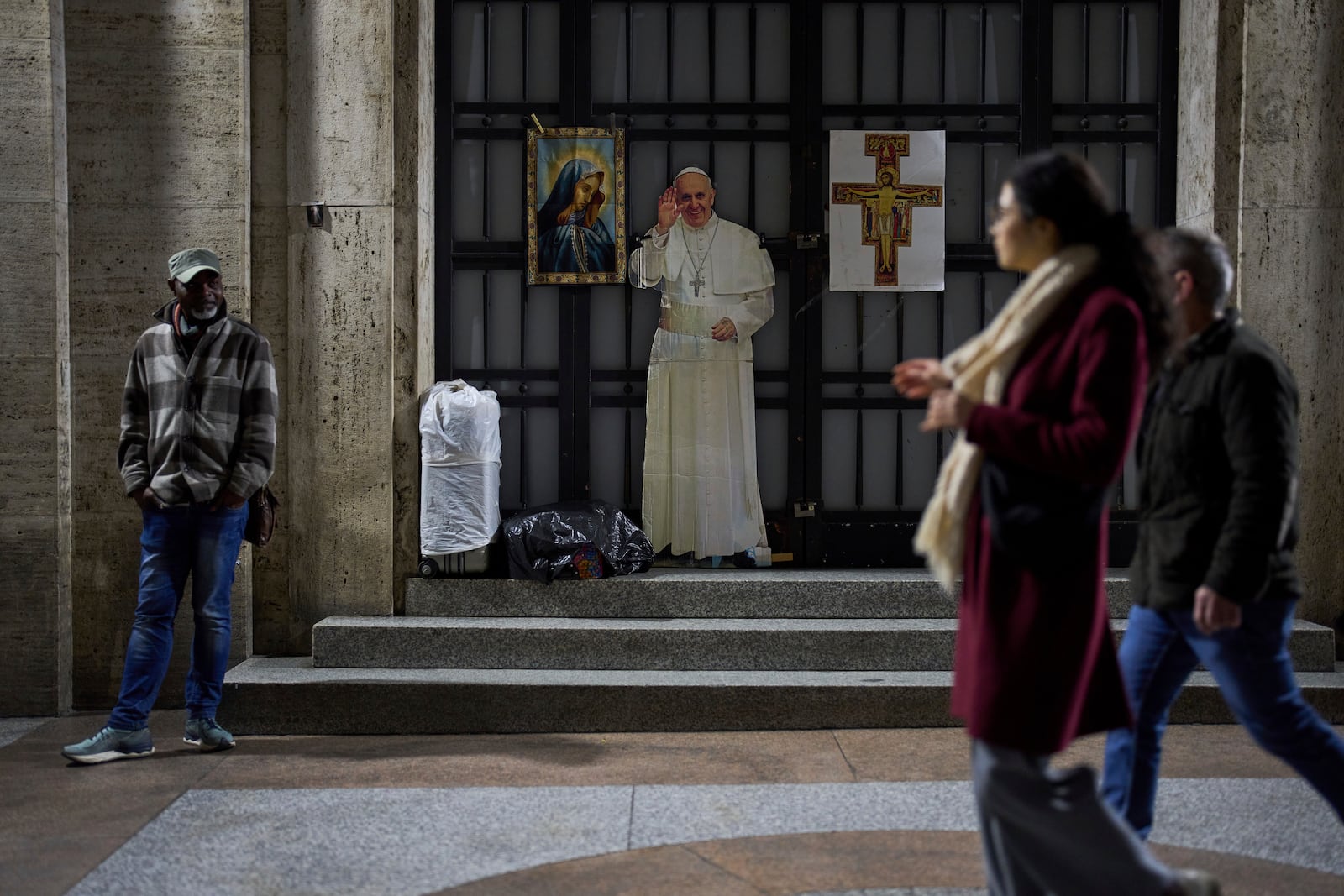 People walk past a cardboard with the image of Pope Francis near St. Peter's Square in Rome, Saturday, March 8, 2025. (AP Photo/Francisco Seco)