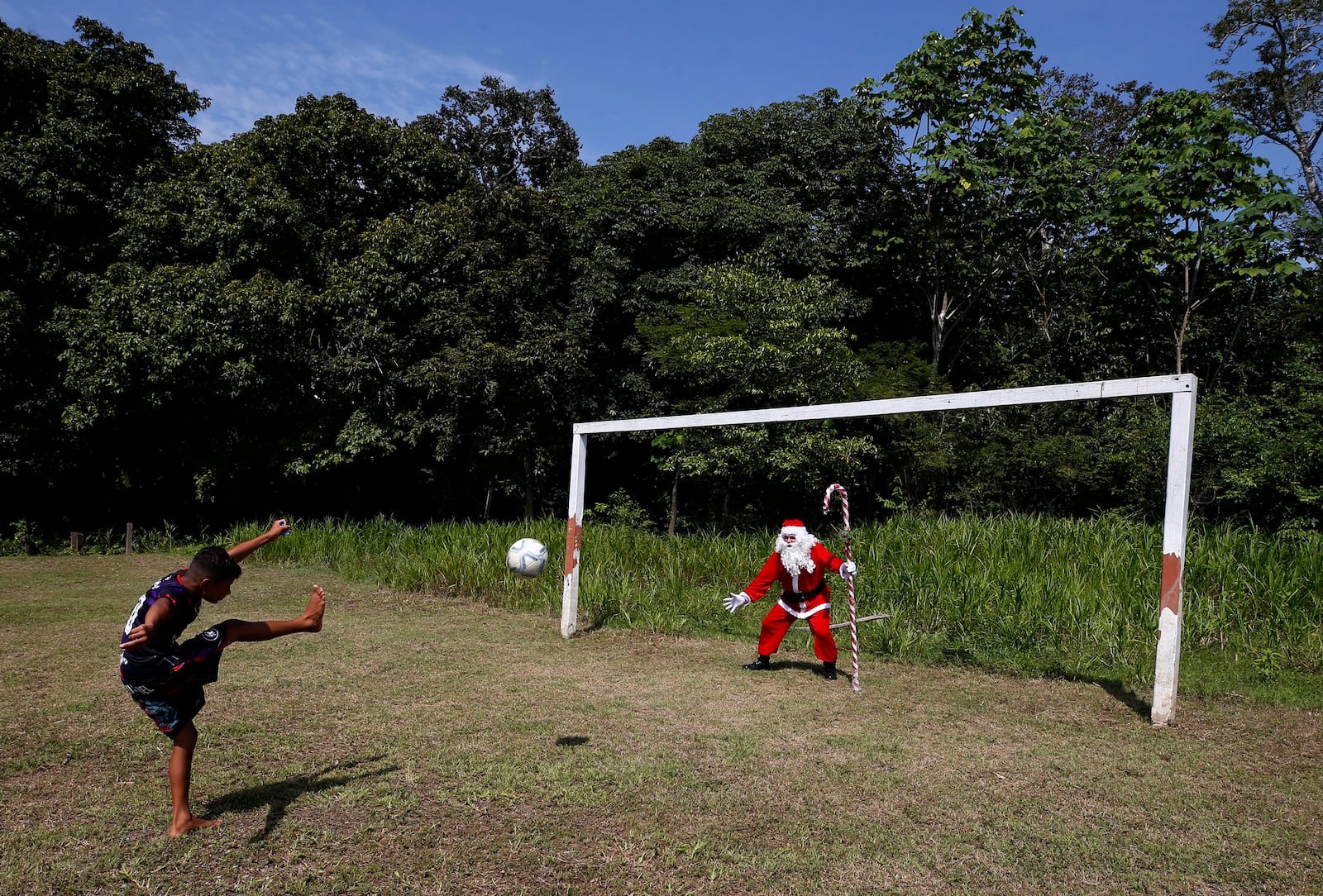 A young Amazonian resident strikes a ball towards Jorge Barroso, dressed as Santa Claus, who gave the ball to the boy after Barroso arrived on a boat to distribute Christmas gifts to children, in Iranduba, Brazil, Saturday, Dec. 21, 2024. (AP Photo/Edmar Barros)