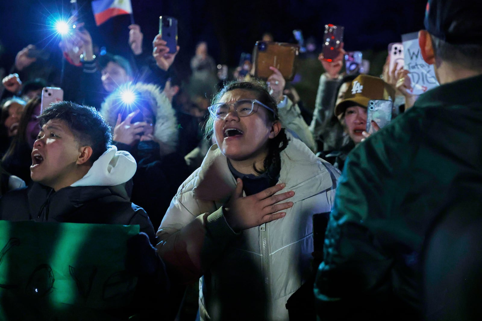 Supporters of former Philippine President Rodrigo Duterte hold up their phones and wave flags during a demonstration outside the International Criminal Court detention center near The Hague in Scheveningen, Netherlands, Wednesday, March 12, 2025. (AP Photo/Omar Havana)