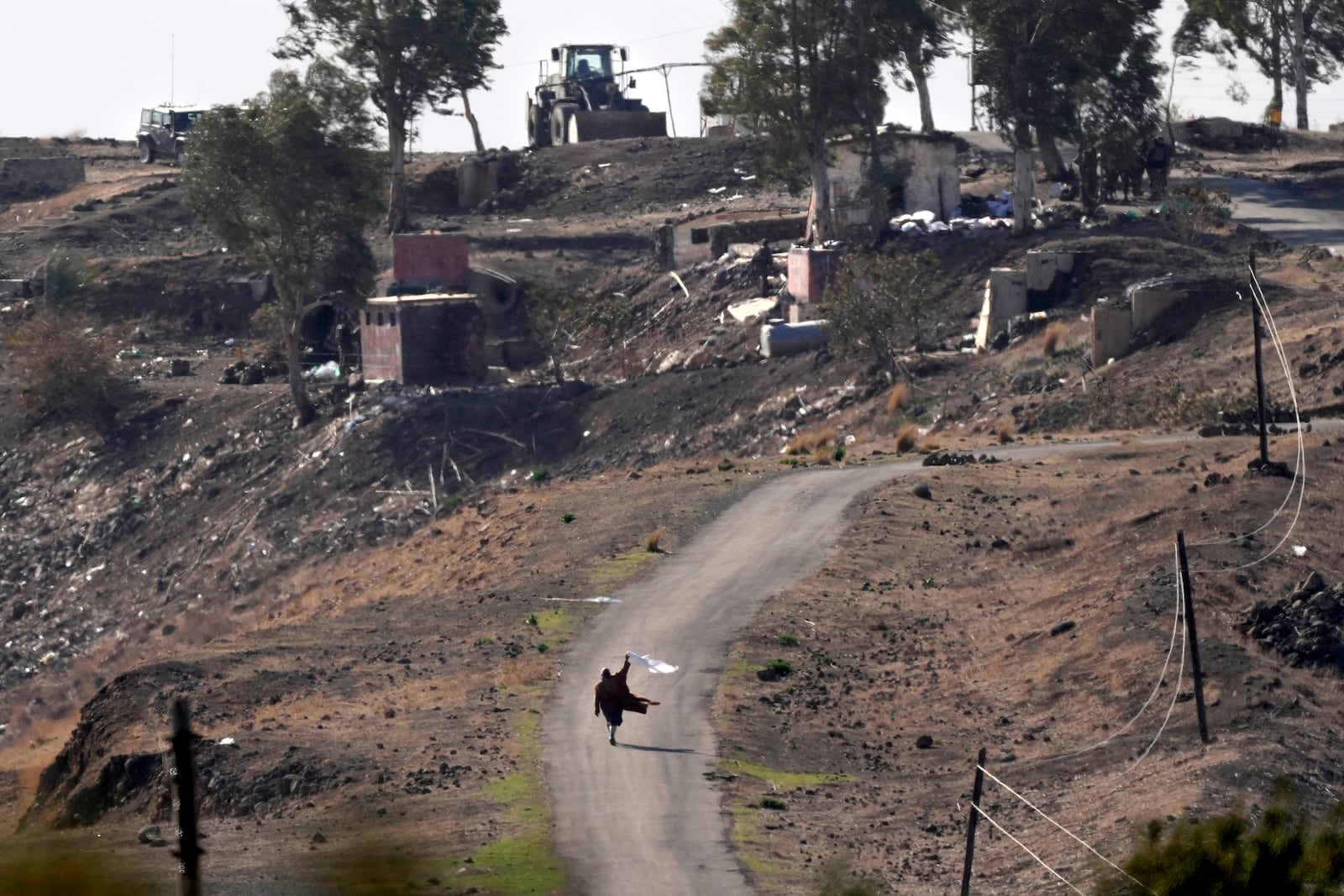 A Syrian man waves a white flag, as he approaches Israeli soldiers to negotiate with them, where they set their new position at an abandoned Syrian military base, in Maaryeh village near the border with Israel in southern Syria, Thursday, Dec. 19, 2024. (AP Photo/Hussein Malla)