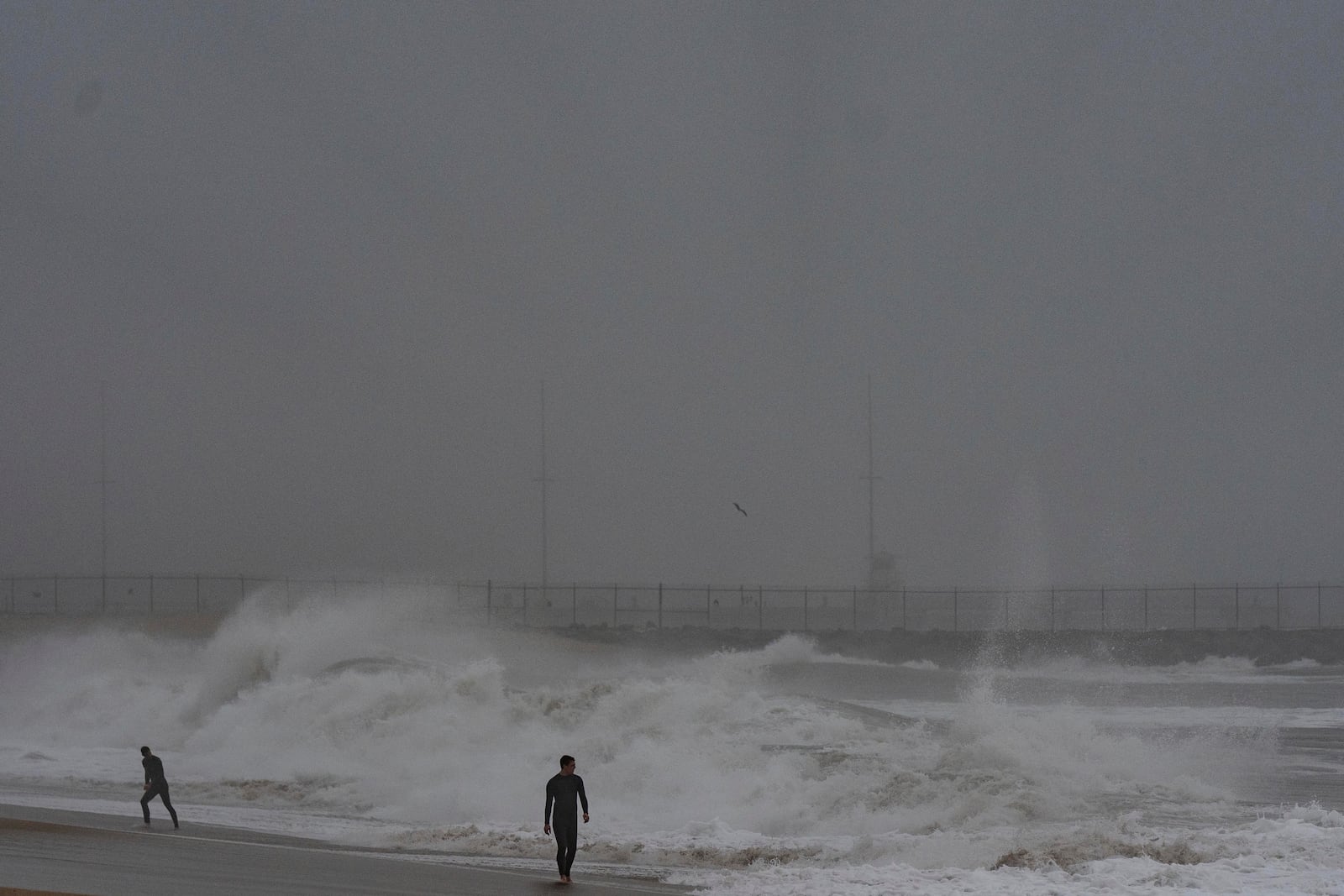 Two surfers walk along the beach as waves crash in Seal Beach, Calif., Tuesday, Dec. 24, 2024. (AP Photo/Jae C. Hong)