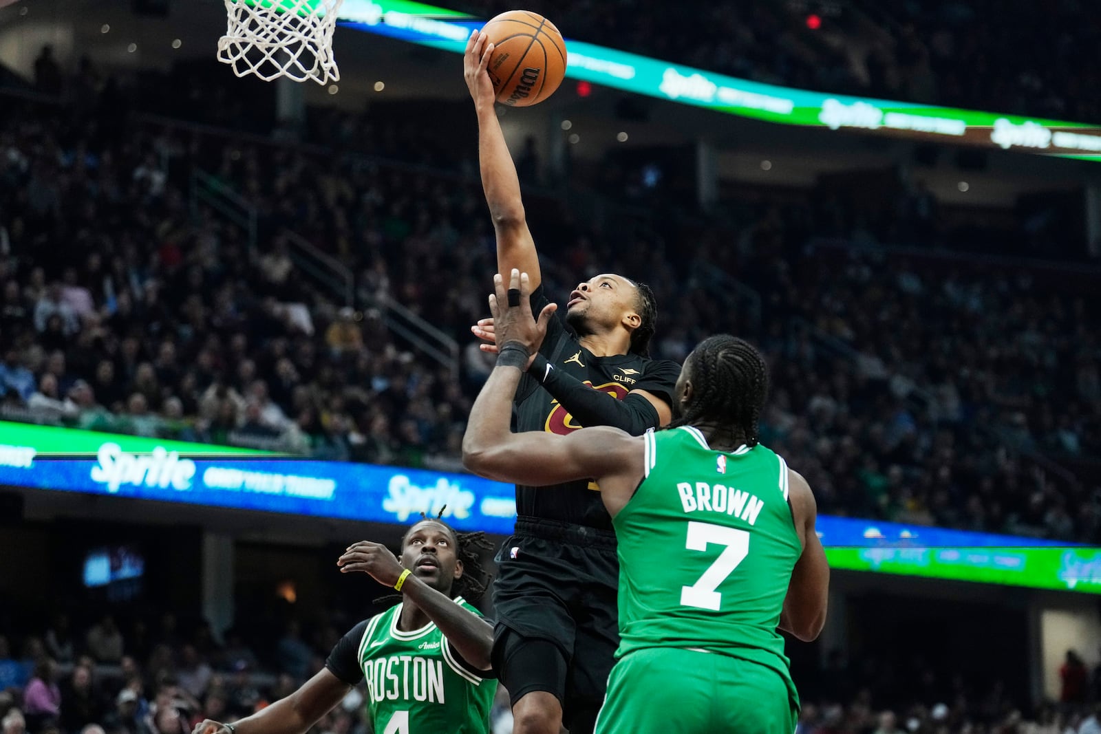 Cleveland Cavaliers guard Darius Garland, center, shoots between Boston Celtics guard Jrue Holiday, left, and guard Jaylen Brown (7) in the first half of an NBA basketball game, Tuesday, Feb. 4, 2025, in Cleveland. (AP Photo/Sue Ogrocki)