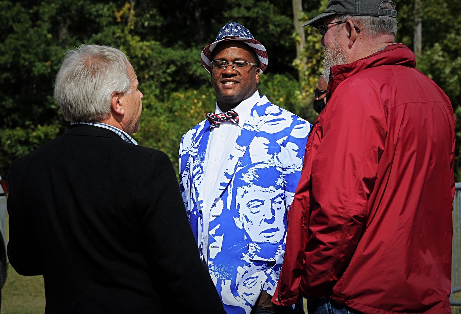 Osie Thomas, center, waited on Monday, Sept. 21, 2020, to see President Donald Trump speak at a hangar at Dayton International Airport. Asked what he hopes to hear today, Thomas – wearing a sports coat covered with images of Trump and Trump socks – mentioned he economy, veterans, the stock market, the coronavirus vaccine, supporting law enforcement, freedom of speech, abortion, the Second Amendment and religion.