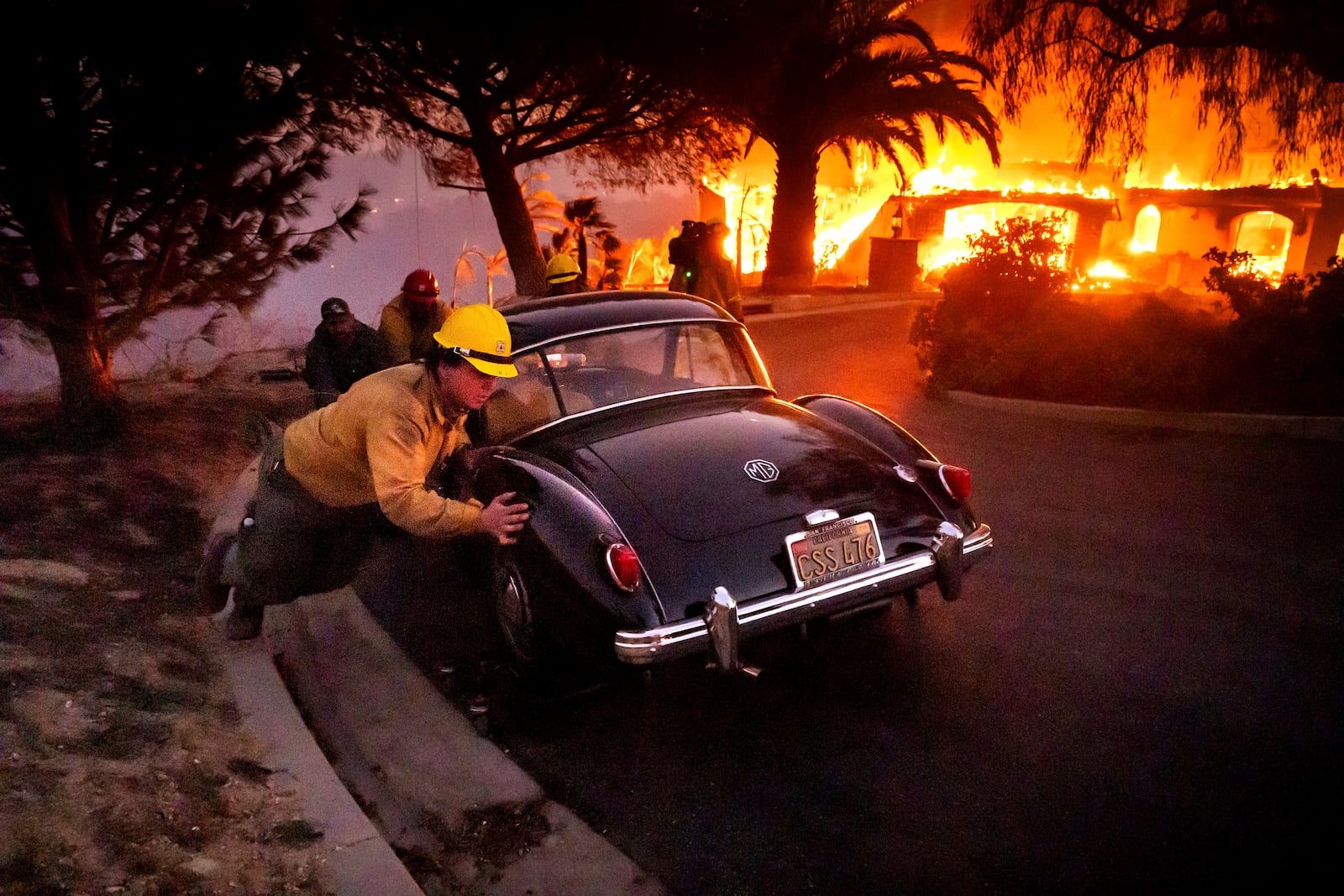 Firefighters and sheriff's deputies push a vintage car away from a burning home as the Mountain Fire burns in Camarillo, Calif., on Wednesday, Nov. 6, 2024. (AP Photo/Noah Berger)