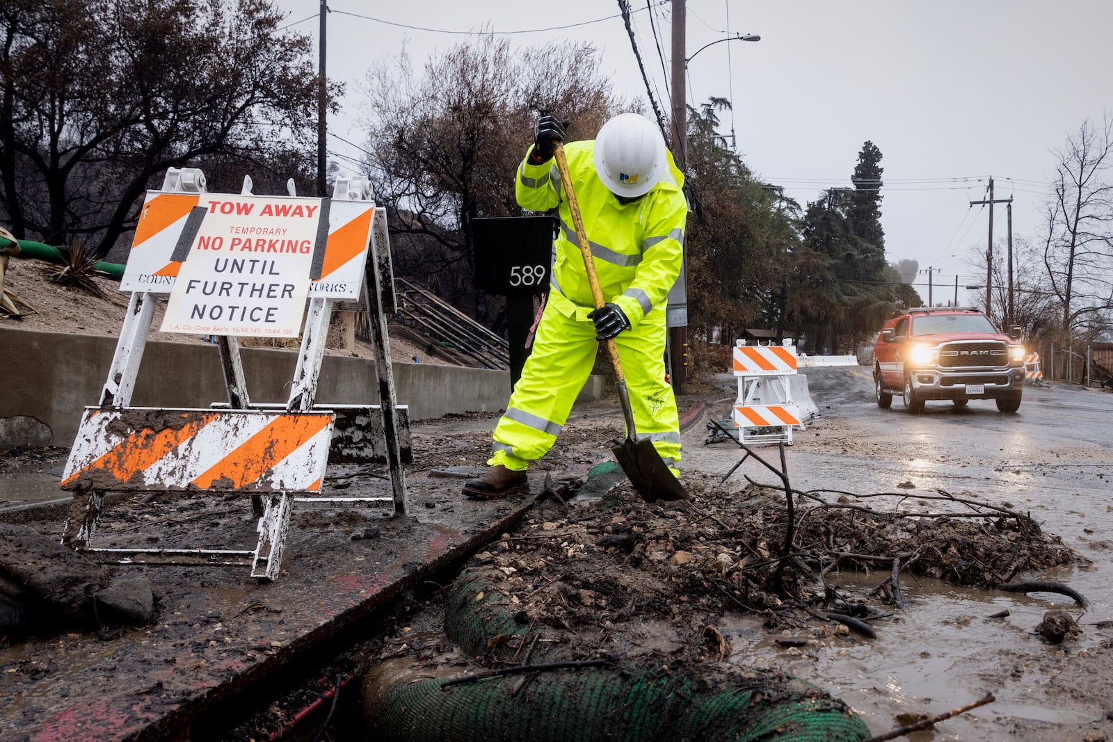 A worker clears debris from a rain gutter in the Eaton Fire zone during a storm Thursday, Feb. 13, 2025, in Altadena, Calif. (AP Photo/Etienne Laurent)