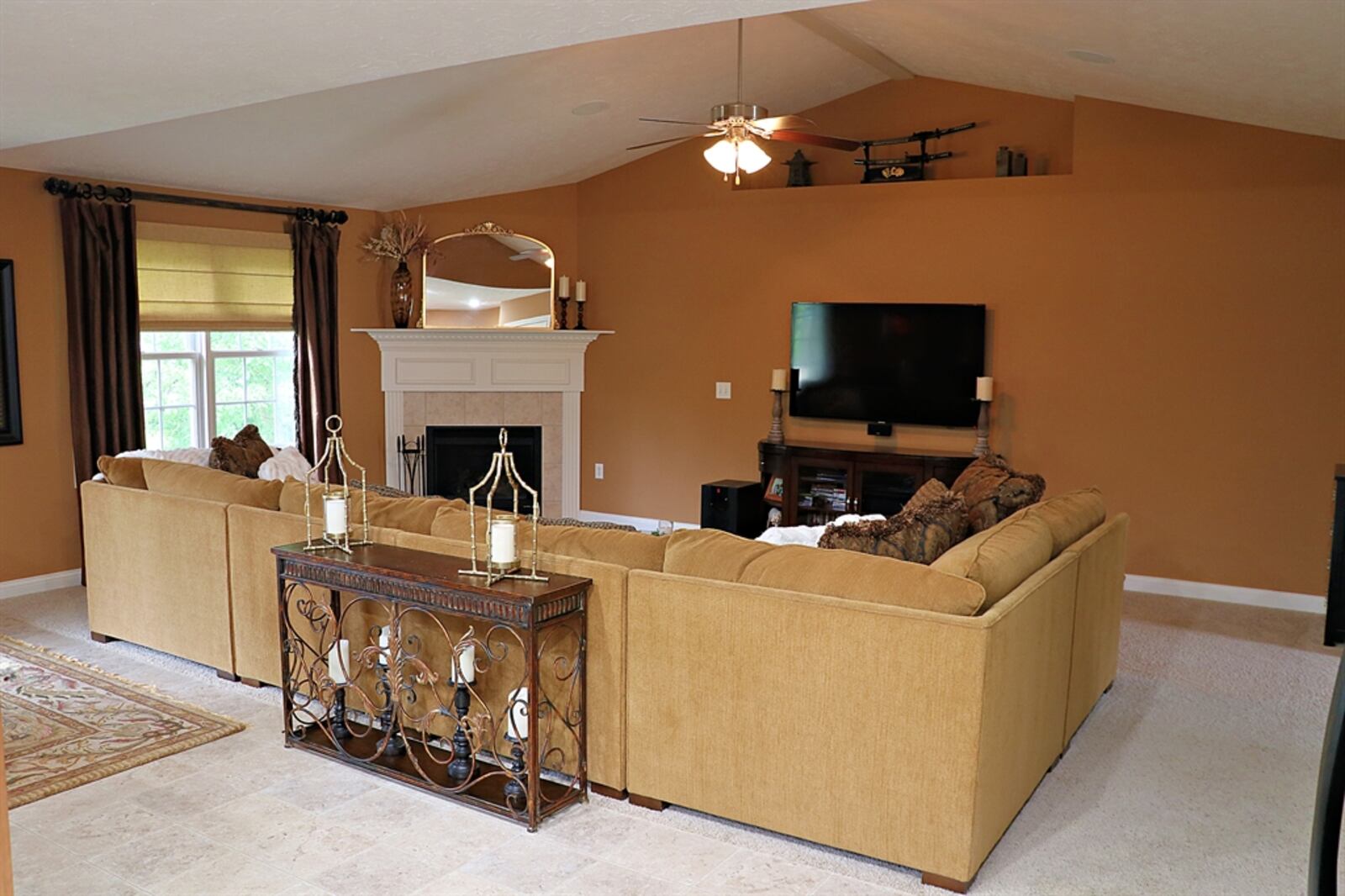 The great room has a cathedral ceiling and plush carpeting. Tucked into one corner is a gas fireplace with a dentil wooden mantel and ceramic-tile surround. 