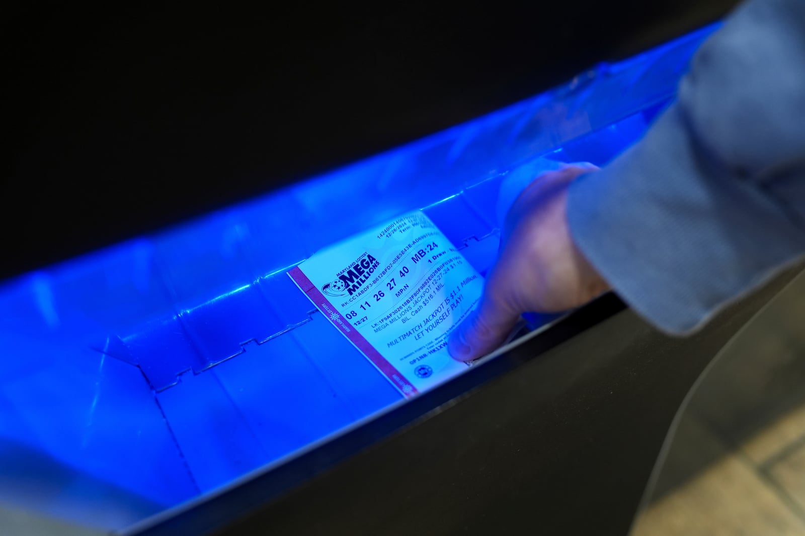 A person retrieves a Mega Millions lottery ticket from a self-serve terminal ahead of Friday's Mega Millions drawing of $1.15 billion, Thursday, Dec. 26, 2024, in Baltimore. (AP Photo/Stephanie Scarbrough)